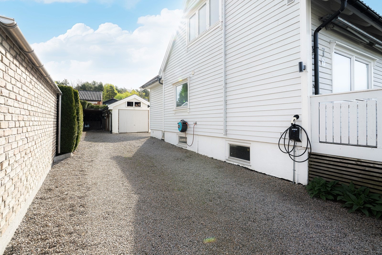 Stor, gruset gårdsplass med ladeboks for elbil og parkering i garasje. Galleribilde