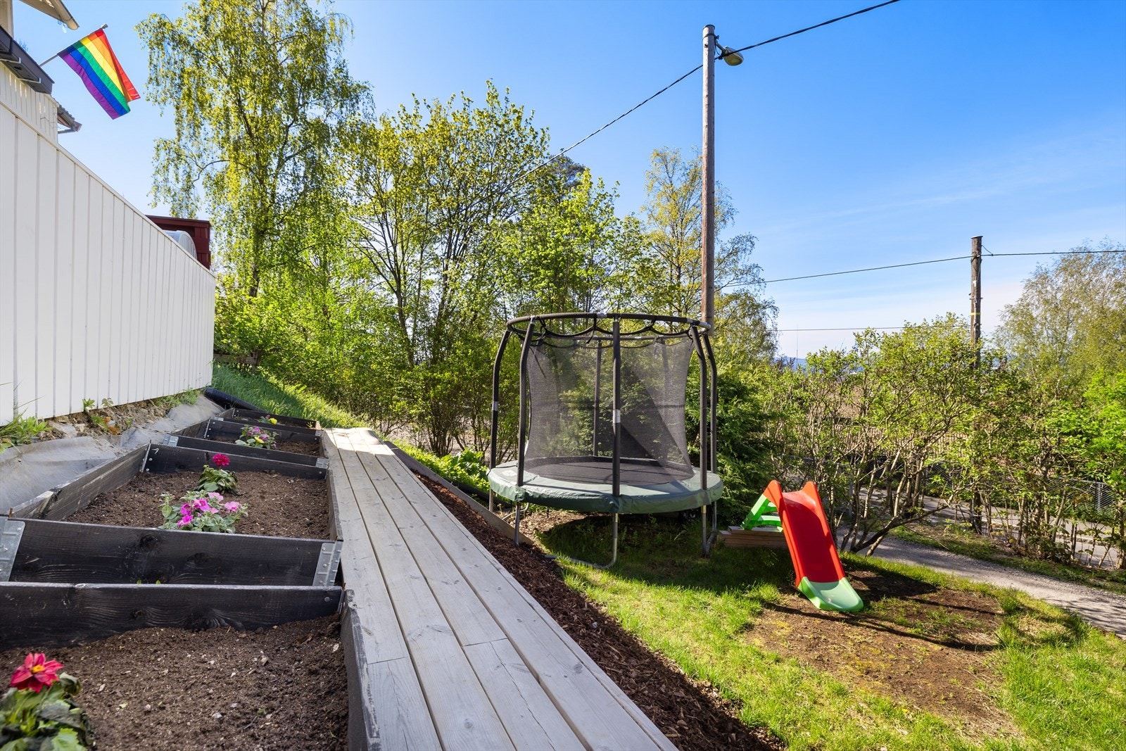 En liten hage med blomster og urtekasser samt plass til trampoline. Galleribilde