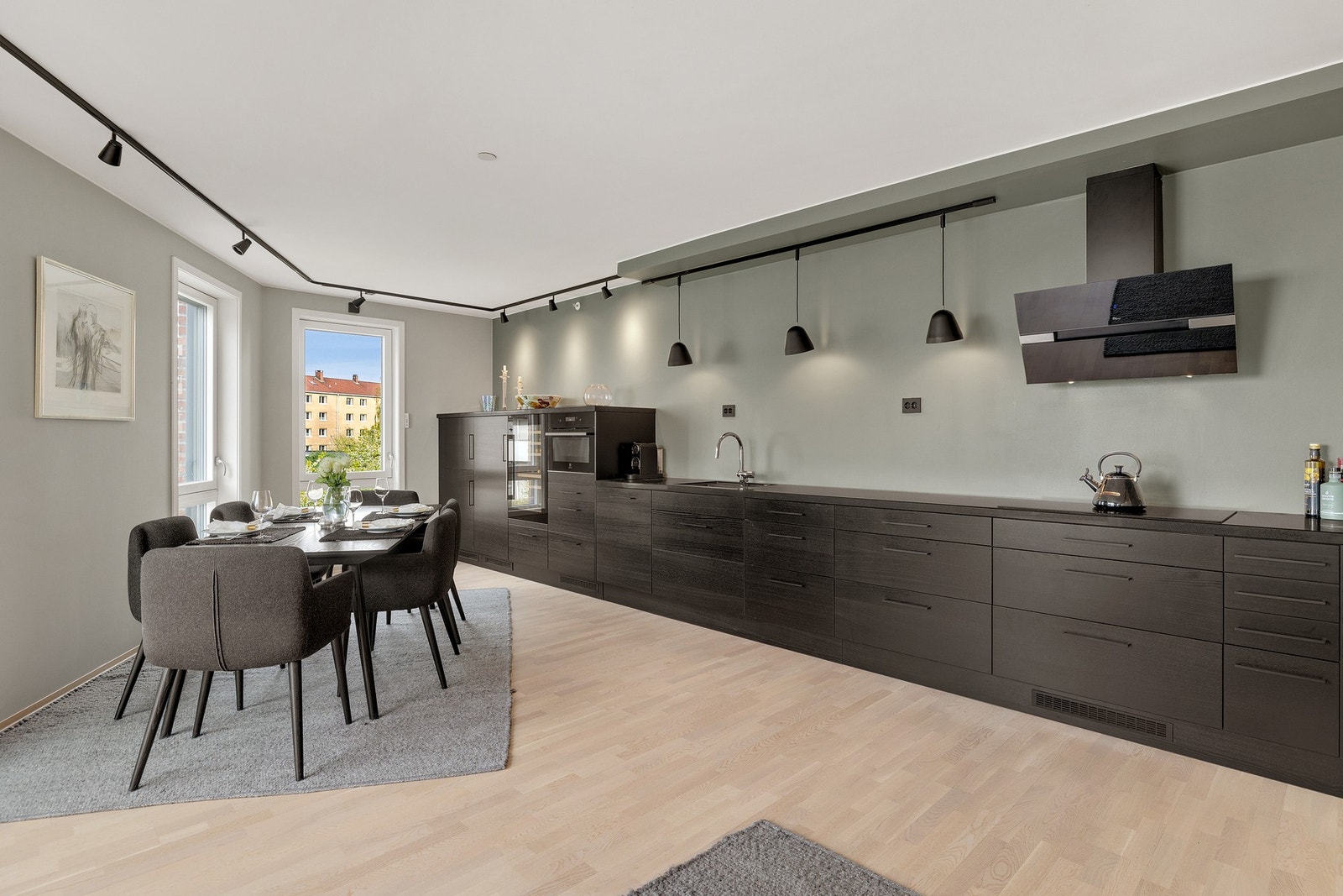 Kjøkkenet fremstår som moderne og stilrent med en helhetlig, mørk innredning som strekker seg langs én vegg i åpen løsning mot stuen. Galleribilde