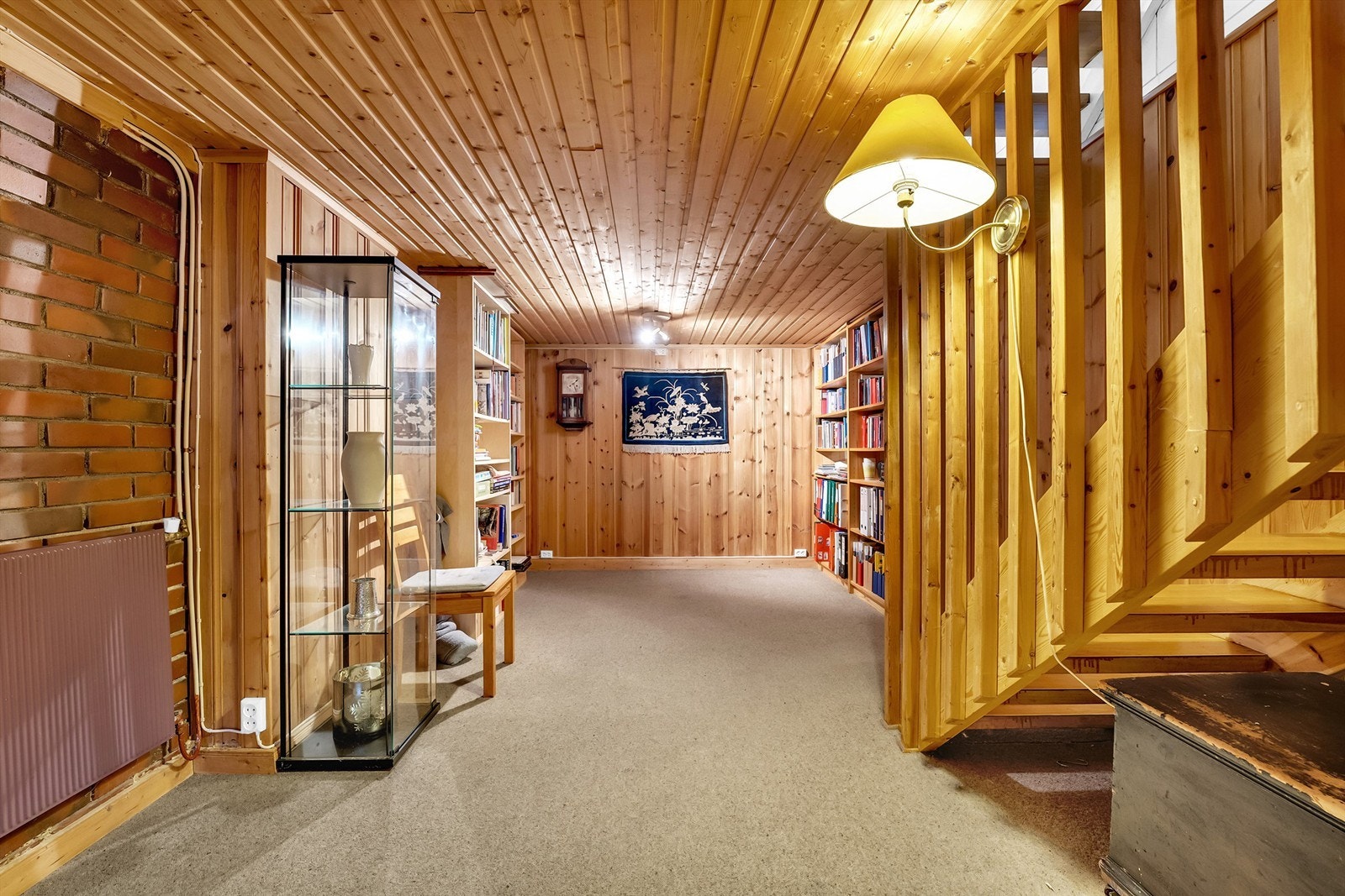 Romslig gang i kjeller ved trappeparti, og gang videre med adkomst til boder og innredet rom som kjellerstue Galleribilde