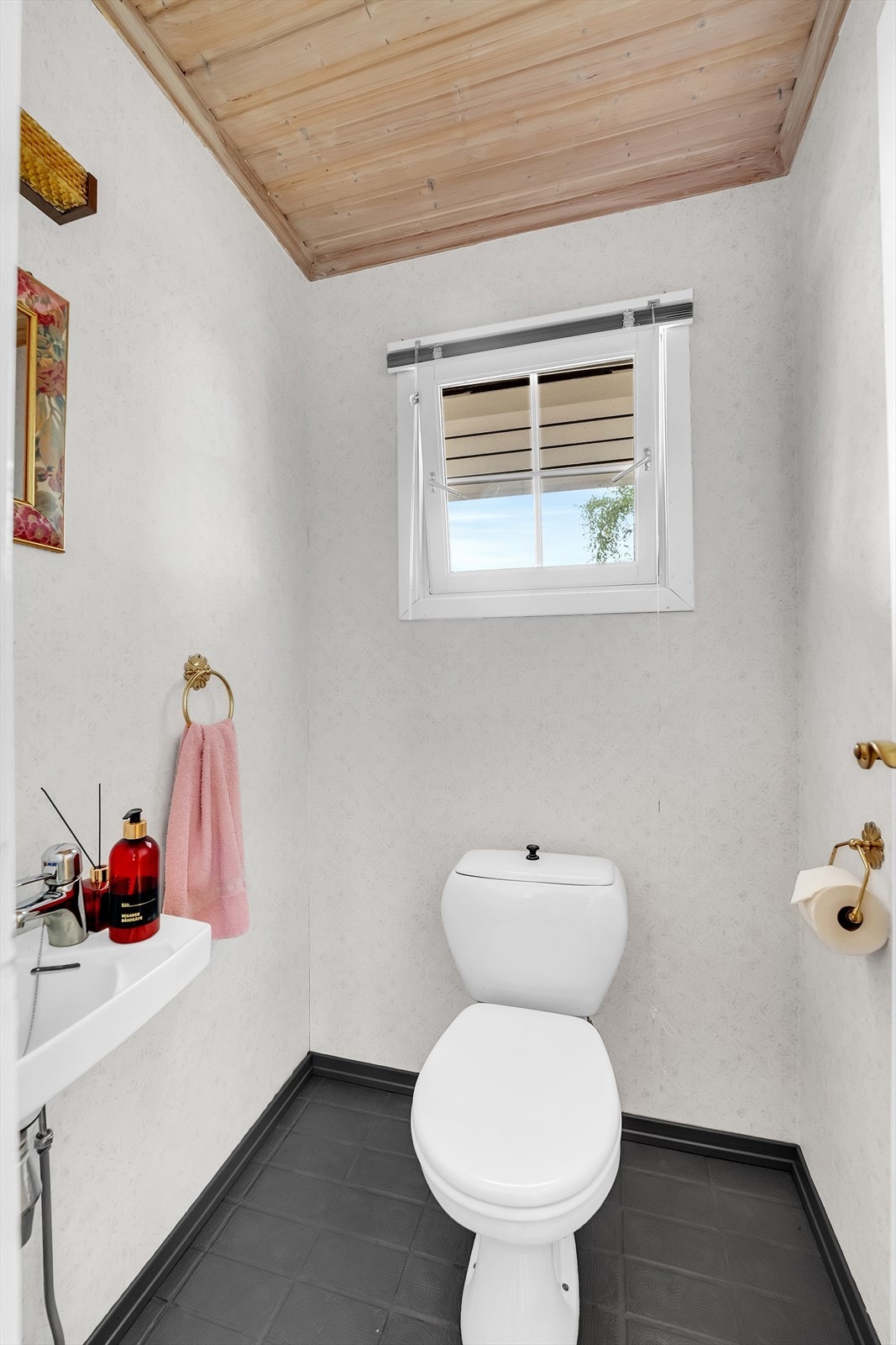 WC-rom i 1.etasje har vegghengt servant med ettgreps armatur, tapetserte vegger, gulvmontert toalett og flisbelagt gulv. Galleribilde