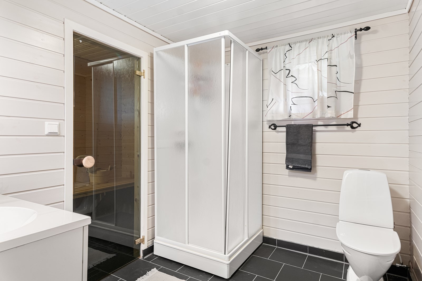 Bad med fliser på gulv som inneholder wc, dusjkabinett. baderomsinnredning i hvit utførelse og varmekabler i gulv for ekstra komfort. Galleribilde