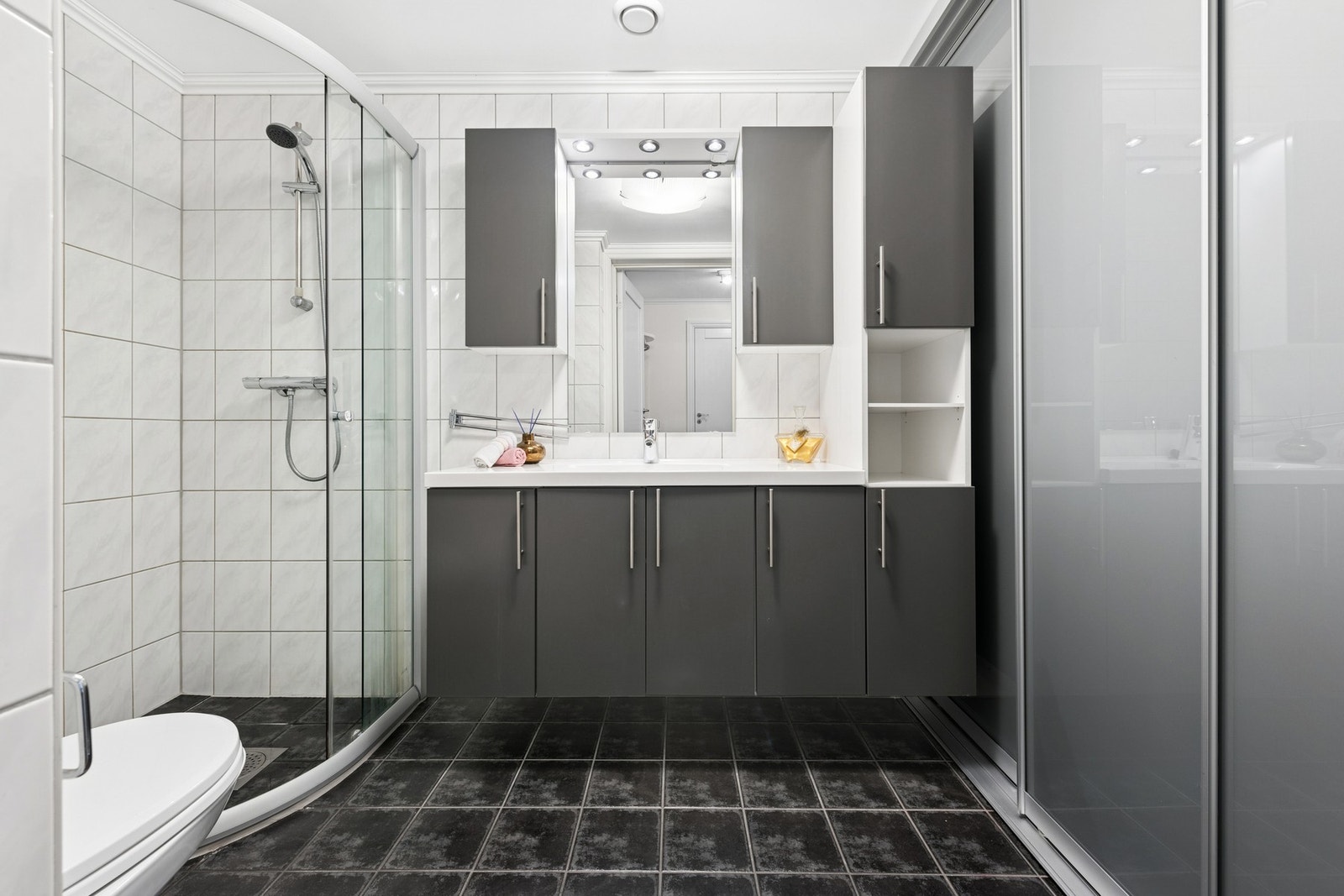 Badet er fra byggeår og har flislagte overflater, gulvvarme og dusjhjørne med glassdører. Galleribilde