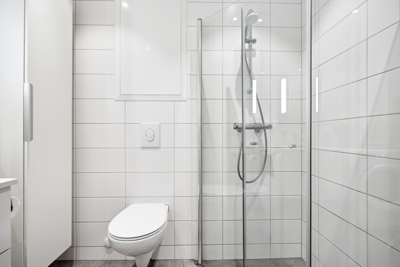 Badet er utstyrt med vegghengt toalett, servantinnredning og dusjhjørne med glassdører, samt opplegg for vaskemaskin. Galleribilde