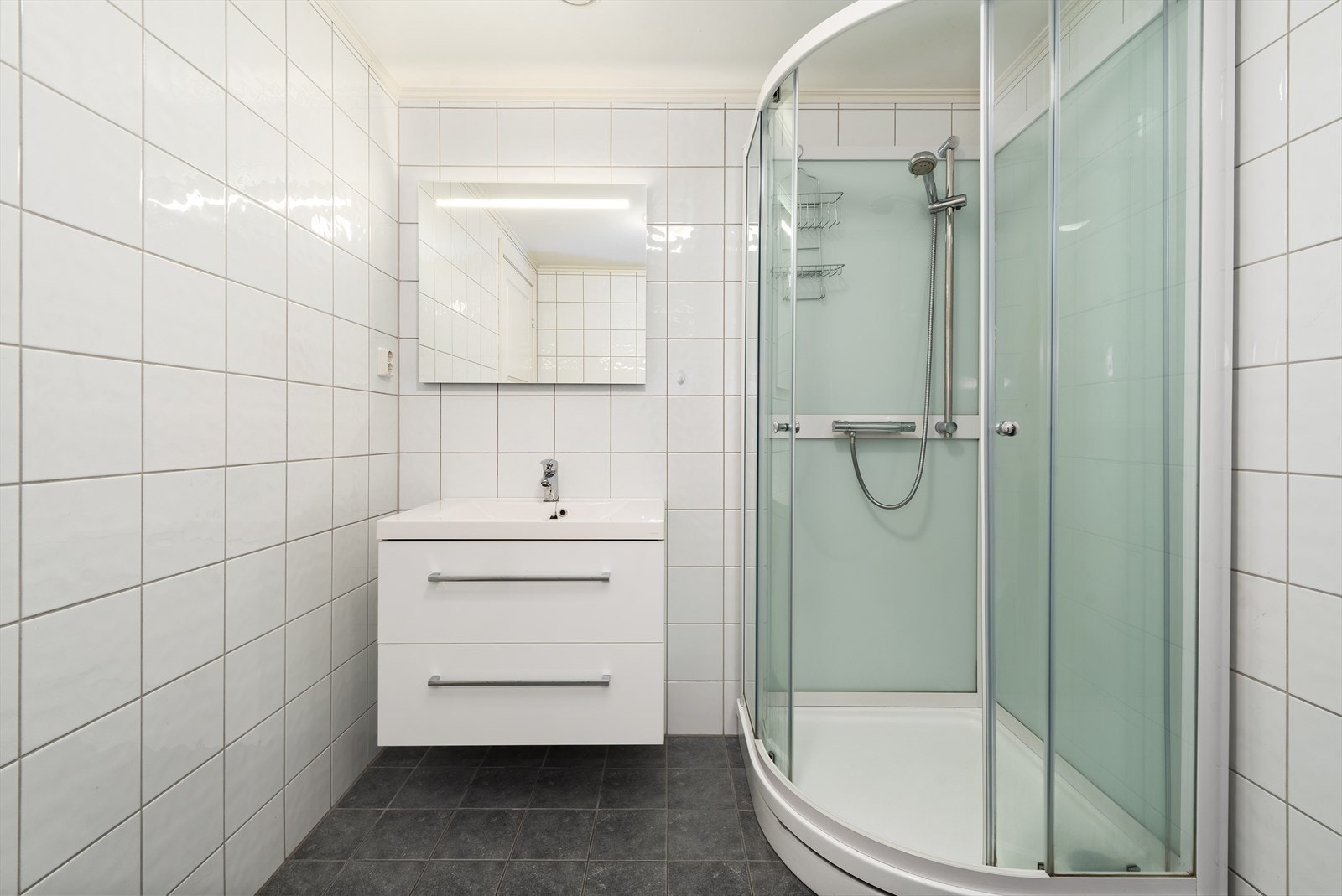 Pent flislagt bad med skuffinnredning, speil m/ integrert lys, dusjkabinett og wc Galleribilde