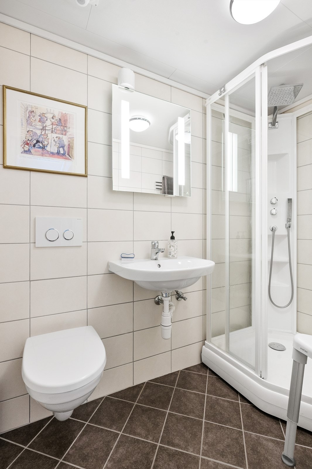 Baderommet i underetasjen har fliser på gulv og vegger og er innredet med servant, klosett med innebygd sisterne, speil med lys og dusjkabinett. Galleribilde