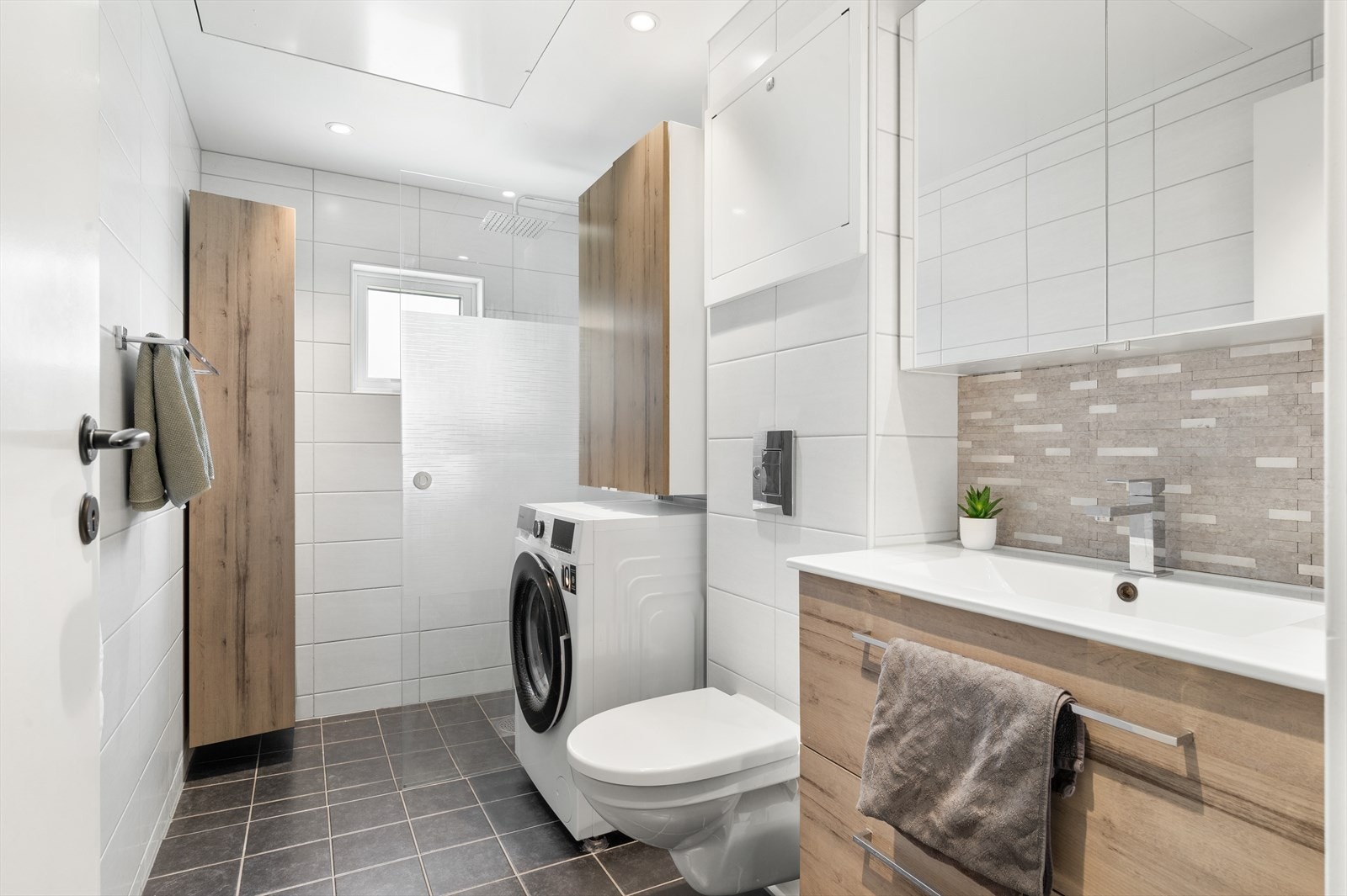 Lekkert helfliset bad, utstyrt med vegghengt toalett, helstøpt servant med skuffer, dusjvegg i klart glass, opplegg for vaskemaskin og fordelerskap til rørsystemet. Varme i gulv. Galleribilde