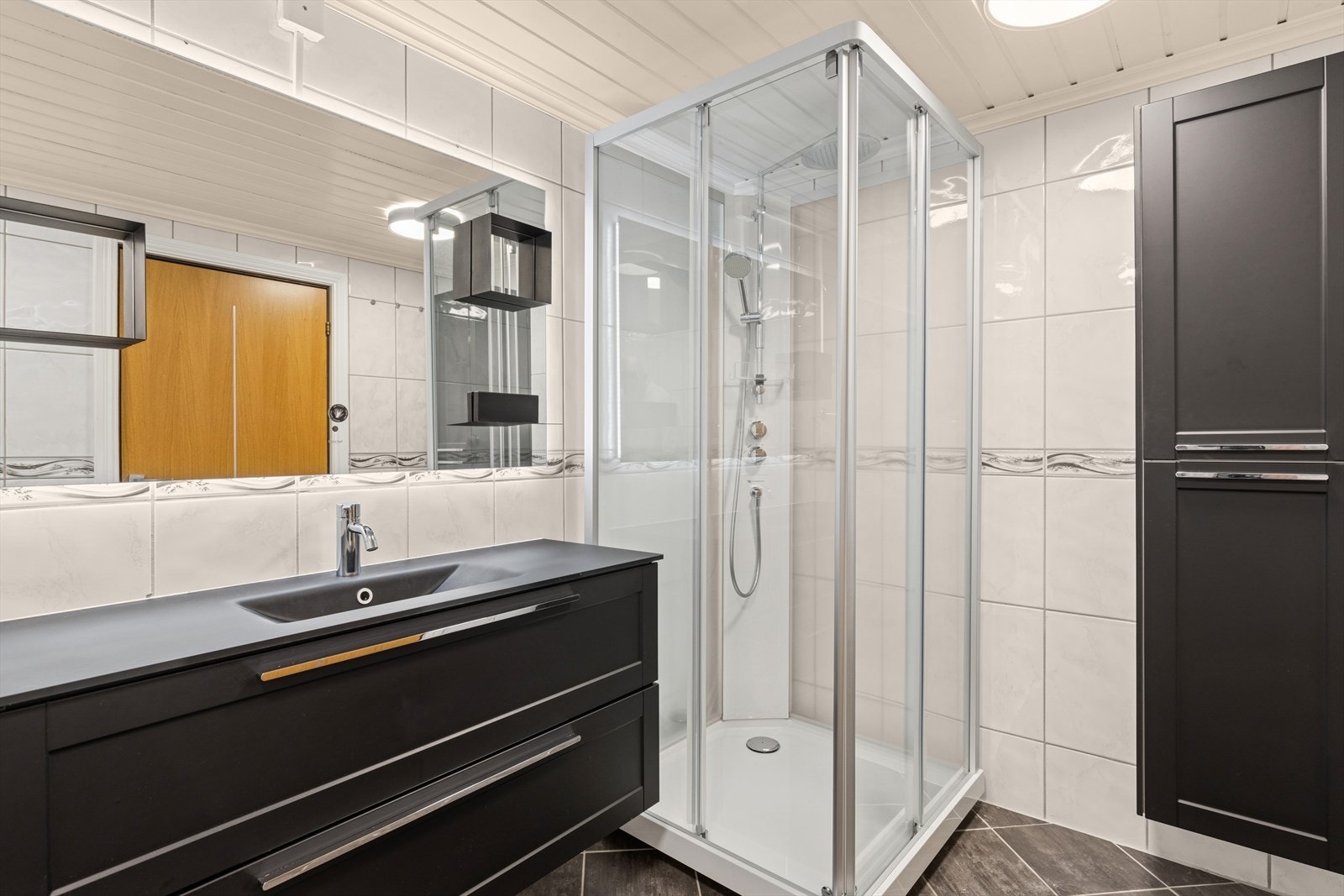 Kombinert bad, wc og vaskerom med flislagte vegger, malt panel i himling og flislagt gulv med gulvvarme. Badet ble oppgradert i ca. 2022 med ny baderomsinnredning og dusjkabinett. Galleribilde