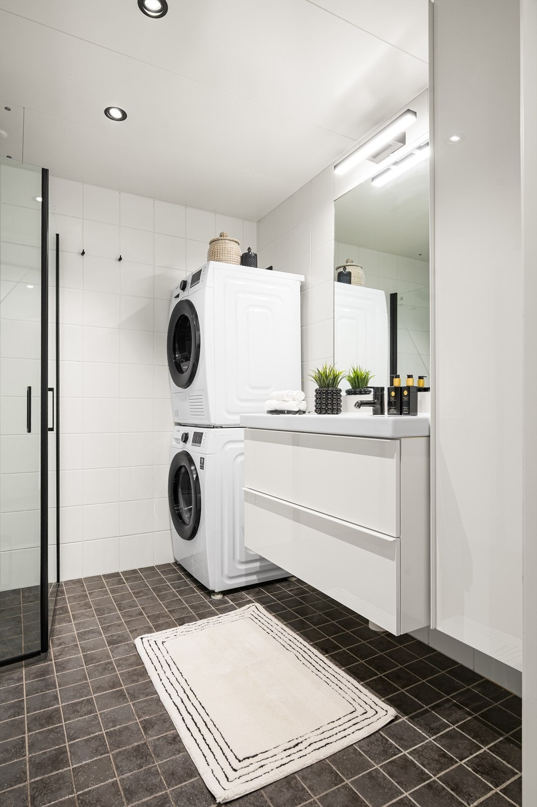 Badet har alt du trenger og er innredet med toalett, servant med underskap, vegghengt speilskap og dusjhjørne med sorte detaljer og svingbare glassdører. Galleribilde