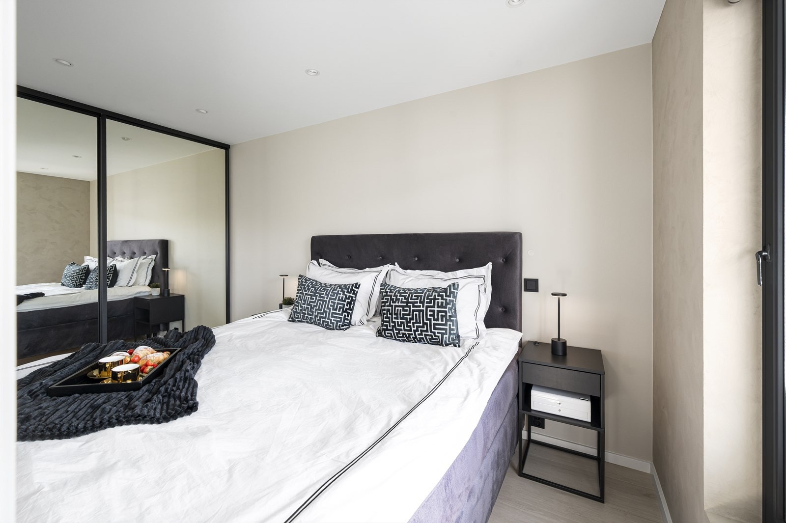 Rommet har god plass til dobbeltseng og nattbord på hver side, og langs den ene veggen er det montert en stor skyvedørsgarderobe med speilfronter som både gir rikelig oppbevaring og ekstra romfølelse. Galleribilde