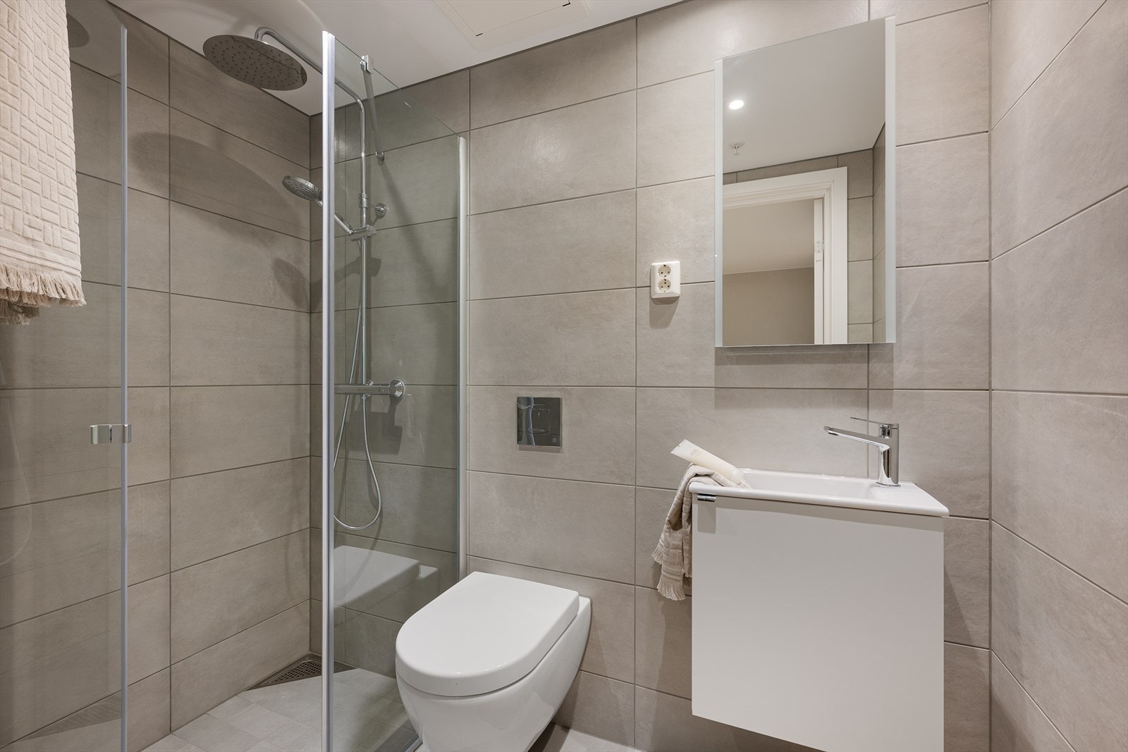 Bad nr. 2 i tilknytning til éntre har flislagte gulv og vegger - Rommet er utstyrt med vegghengt toalett, skapinnredning med ovenpåliggende servant og overhengende speil Galleribilde