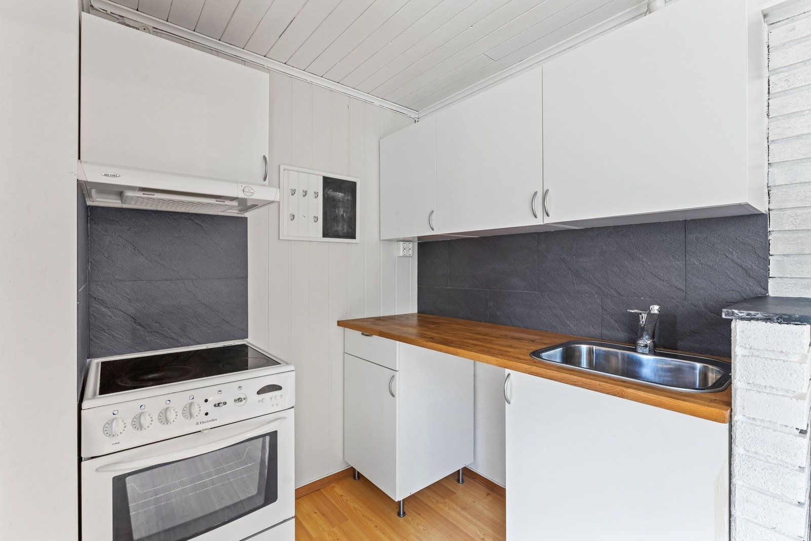 Kjøkkenkroken i kjelleren er utstyrt med laminatbenk, stålkum, fliser mellom benk og overskap, avtrekk og plass til komfyr, kjøleskap og oppvaskmaskin. Galleribilde