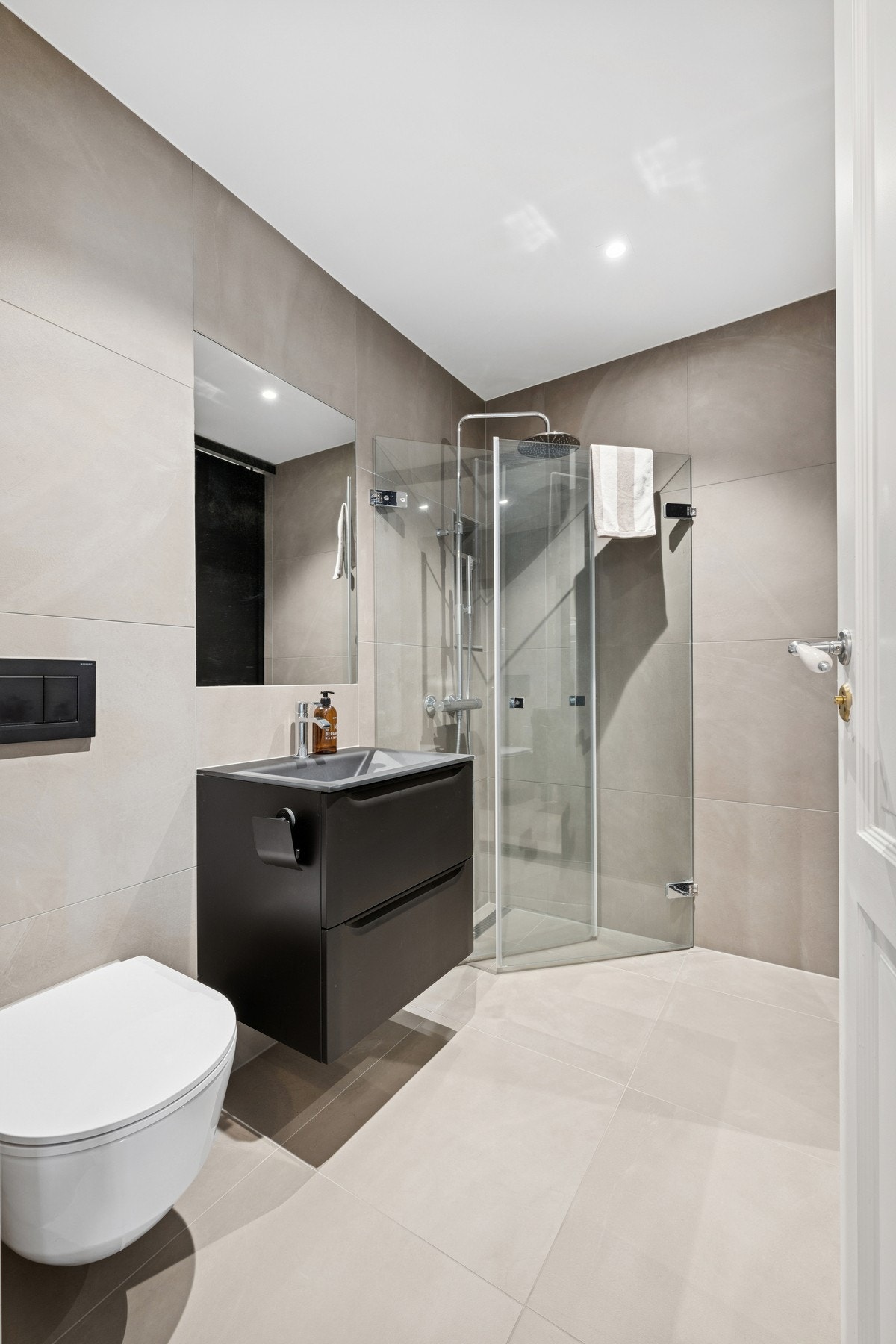 Stilrent og delikat bad med moderne flisvalg, vegghengt toalett, dusjhjørne med regnfallsdusj og praktisk baderomsinnredning i mørke toner. Galleribilde