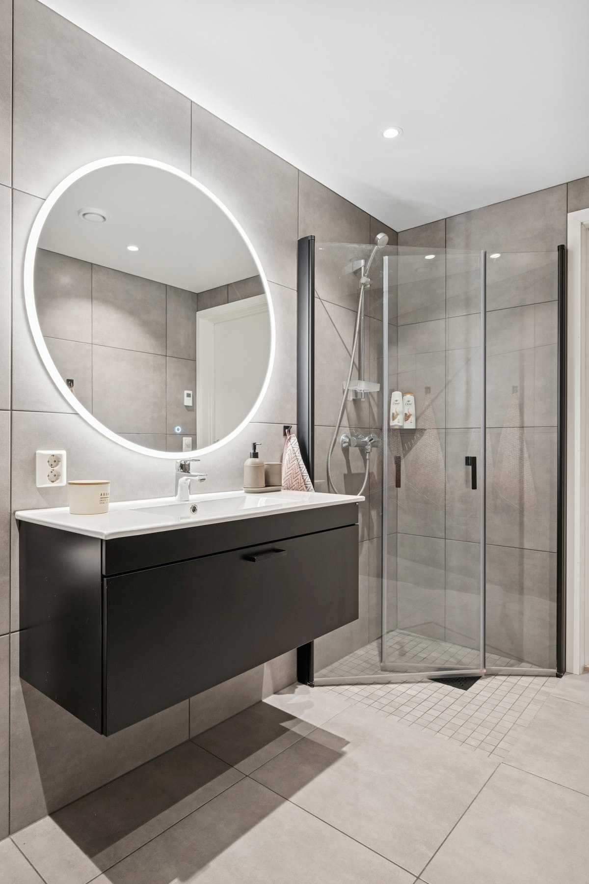 Baderommet er utstyrt med moderne servantinnredning med heldekkende servanttopp, vegghengt speil med integrert belysning, vegghengt toalett og dusjhjørne med svingbare glassdører. Galleribilde