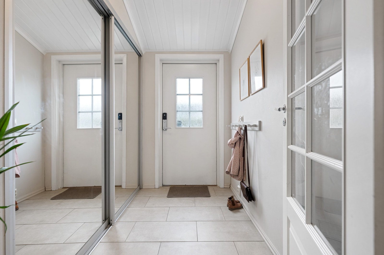 Entré med fliser på gulv, malte vegger i en lys farge og plass til å henge av yttertøy i praktisk skyvedørsgarderobe. Galleribilde