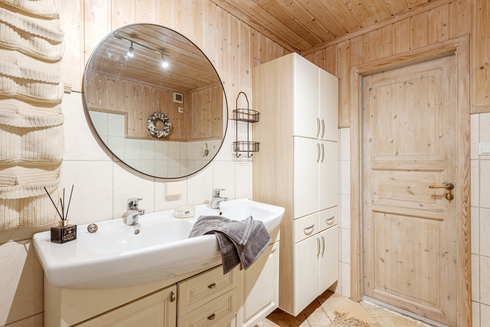 Badet har både et stort dusjkabinett og et badekar med dusjløsning. Grå gulvfliser kombineres med trepanel og hvite fliser på veggene, og badet har toalett, varmekabler og opplegg for vaskemaskin. Galleribilde