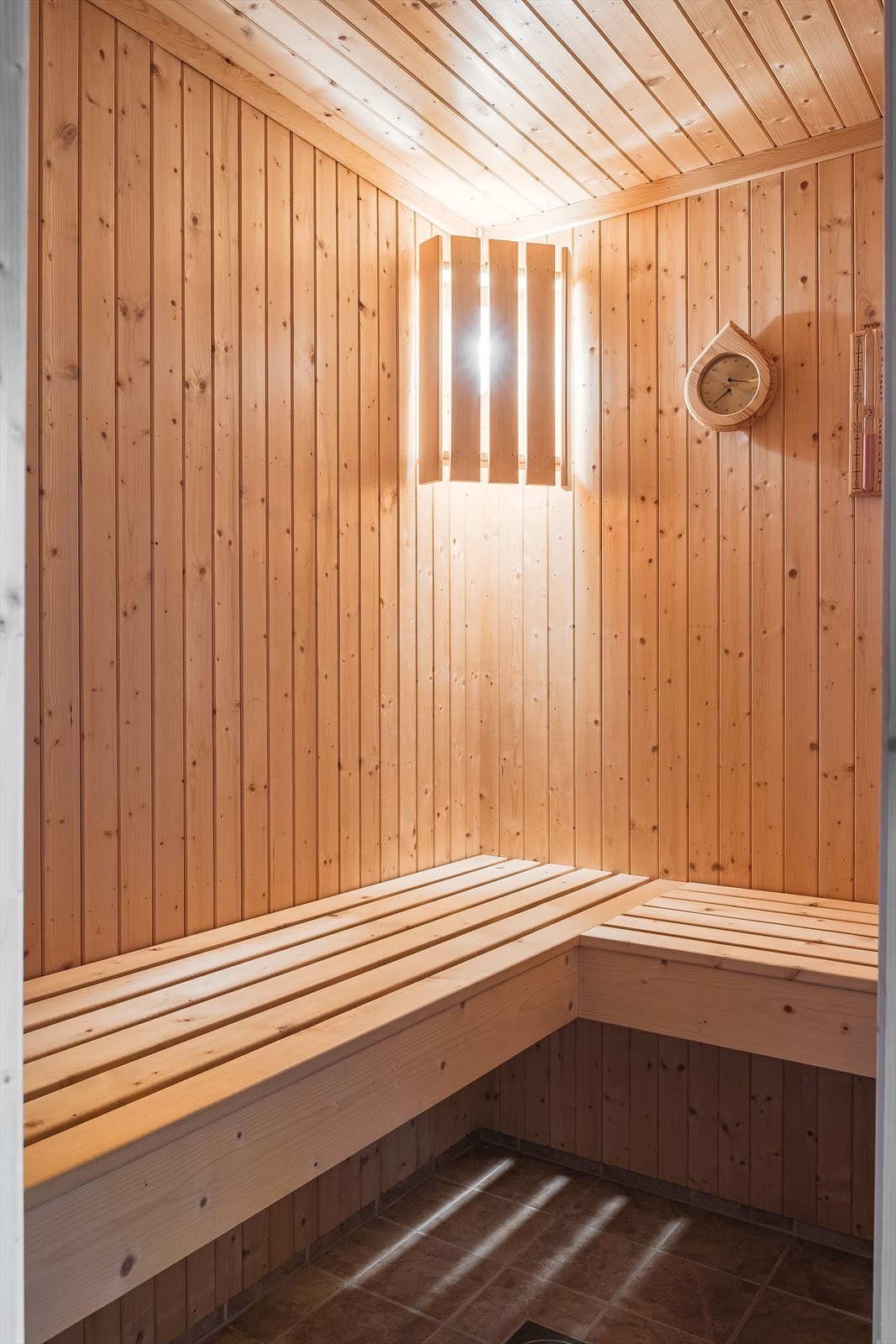 Fra baderommet er det adkomst til en deilig badstue med flislagt gulv, overflater med panel, plassbygget sittebenk og badstueovn av type Tylö. Galleribilde