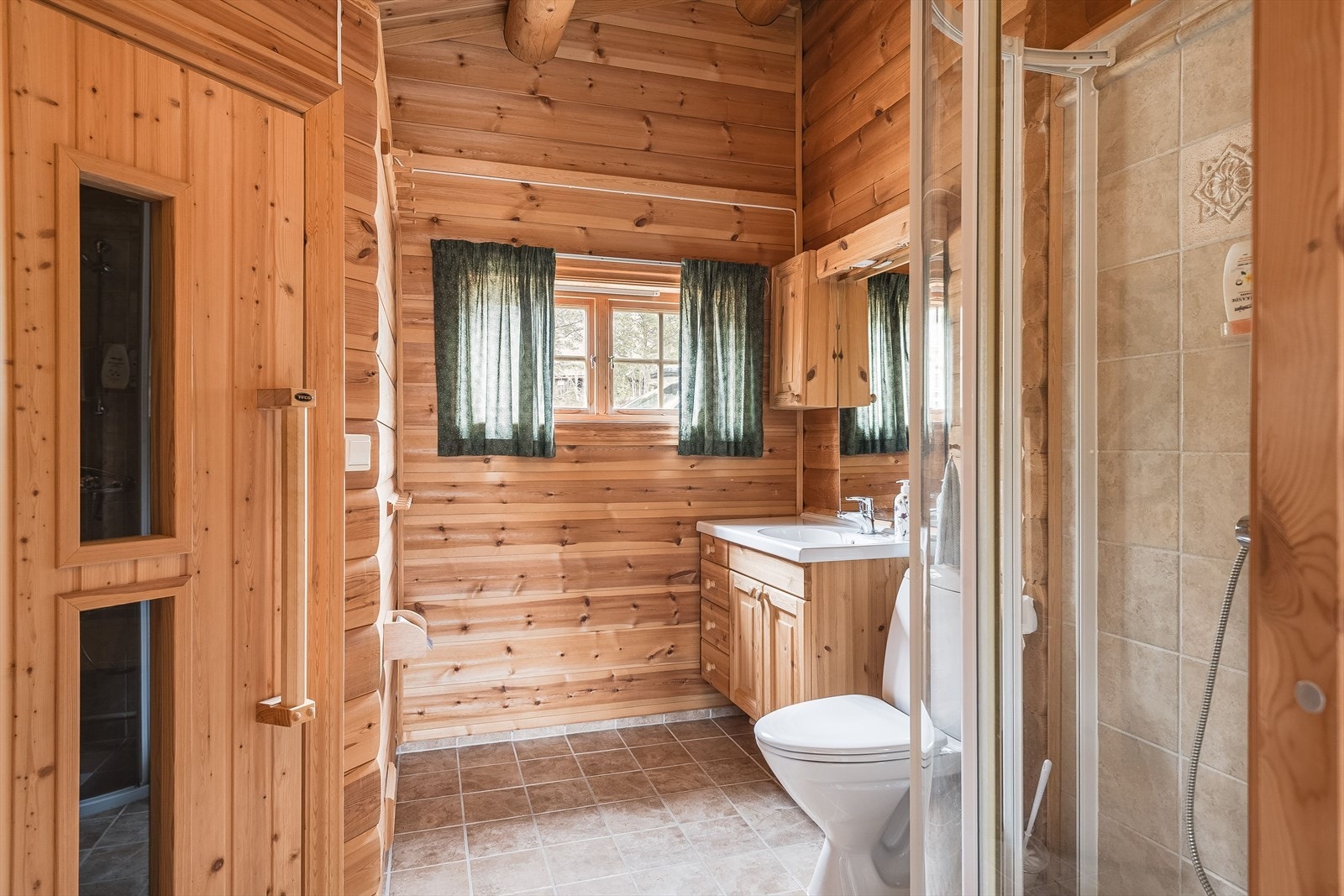 I tilbygget del er det et pent baderom med badstue. Rommet har flislagt gulv med gulvvarme og overflater med maskinlaft kombinert med fliser i dusjen. Galleribilde