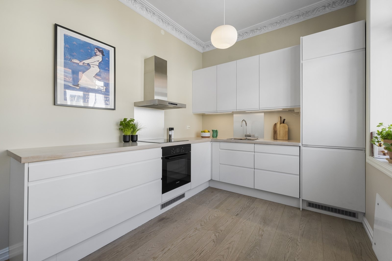 Kjøkkenet har et moderne og stilrent design og funksjonell utforming med lys, tidløs innredning. Den L-formede løsningen består av glatte, hvite fronter og en lys benkeplate som skaper en stilren kontrast Galleribilde