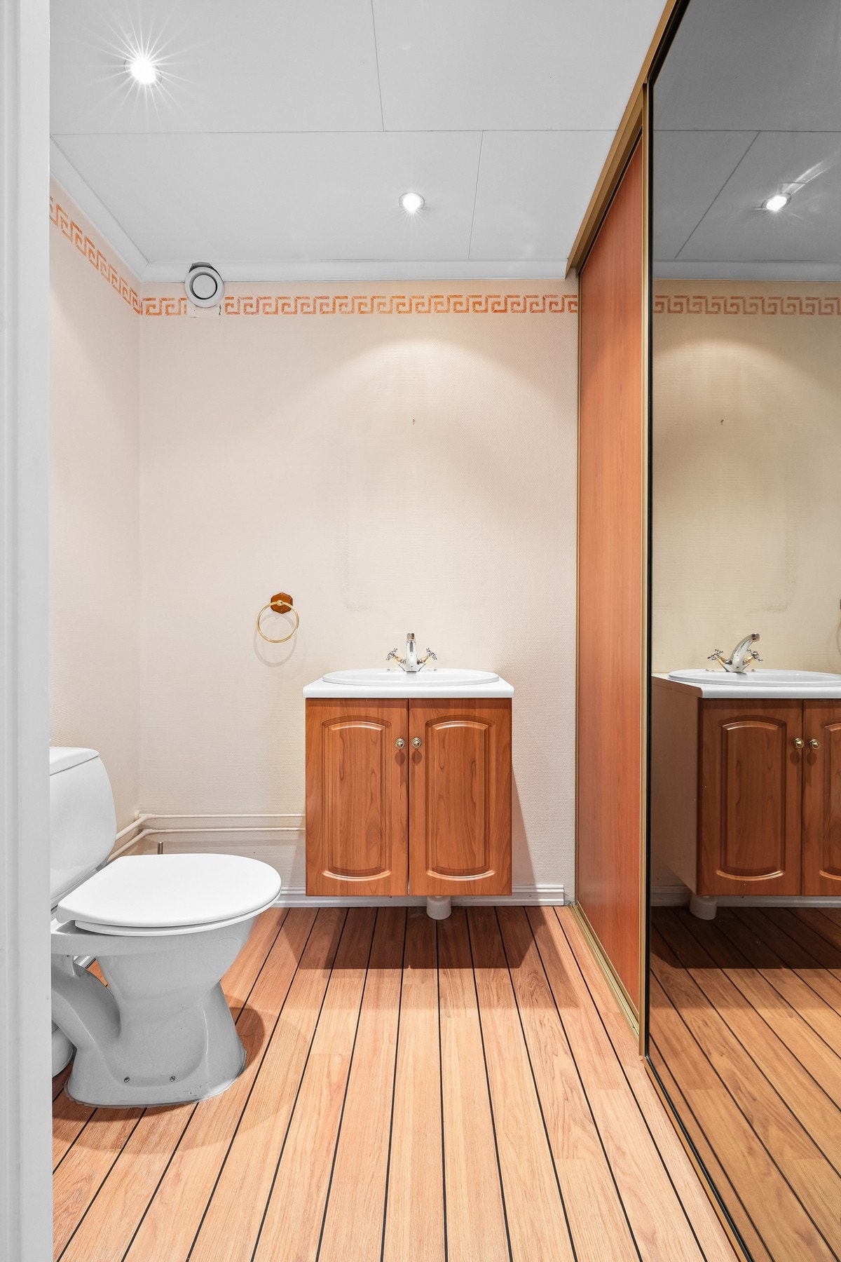 Wc-rommet har linoleumsbelegg på gulvet, lysmalte vegger og gulvmontert toalett. Innredningen består av en servant med underskap, og rommet har også skyvedørsgarderobe. Galleribilde