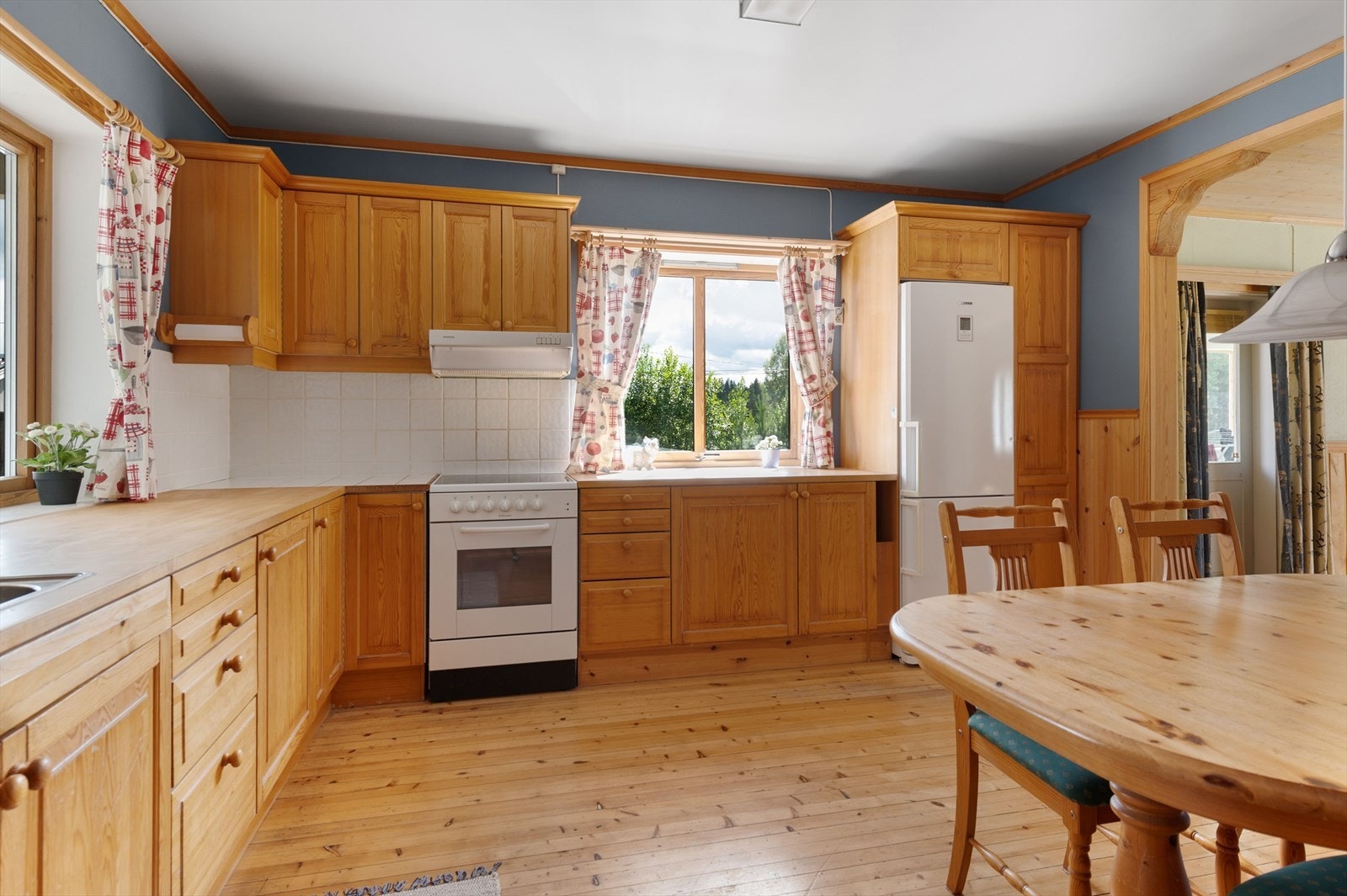 Videre kommer du inn til et hyggelig spisekjøkken. Kjøkkenet har lakkerte tregulv og overflater med brystningspanel kombinert med malt tapet. Galleribilde