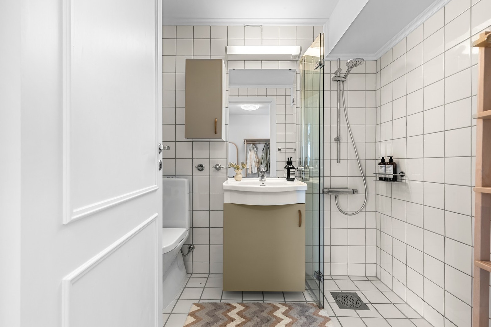 Innredningen består av en heldekkende servant på servantskap, matchende veggskap, speil med overlys, et toalett, og et dusjhjørne med foldbare glassvegger Galleribilde