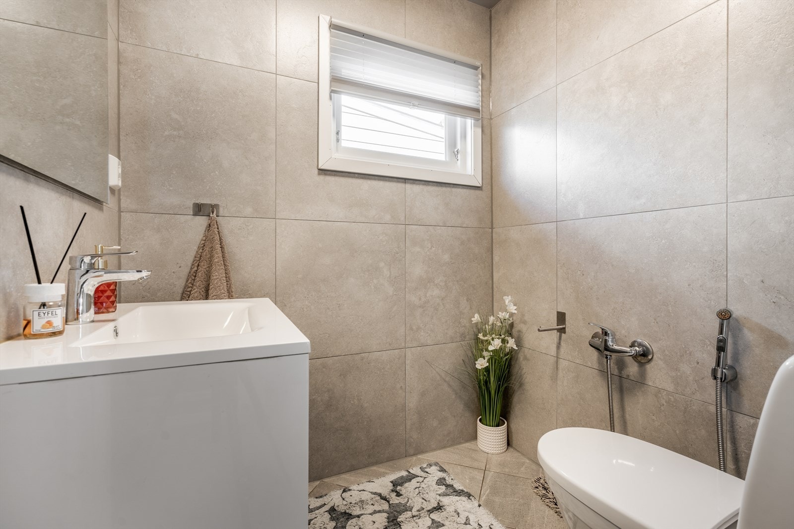 Flislagt toalettrom med gulvvarme som inneholder toalett og servantinnredning med underskuffer og speil. Galleribilde