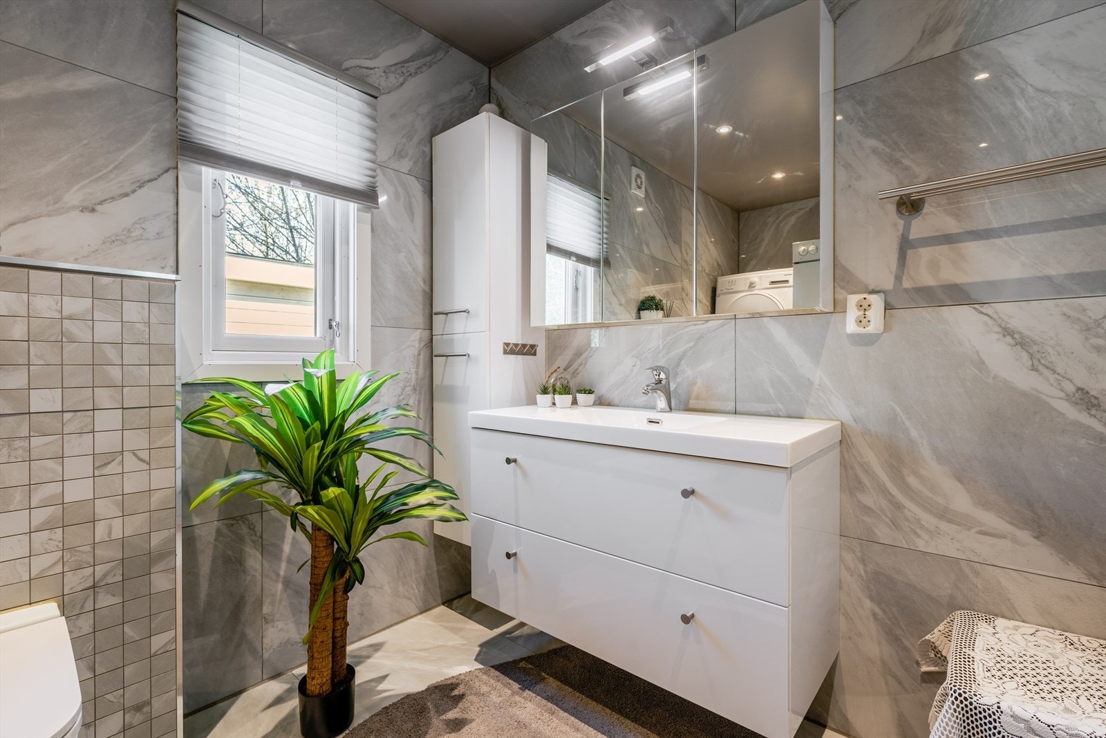 Badet inneholder veggfestet toalett, åpen dusjløsning med dusjdører og servantinnredning med underskuffer, overskap med speildører, overlys samt veggfestet skap. Galleribilde