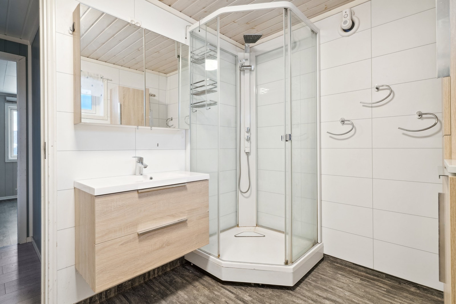 Badet er utstyrt med nedfelt servant med oppbevaringsskap, toalett og dusjkabinett. Ekstra vegghengt skap for praktisk oppbevaring. Galleribilde