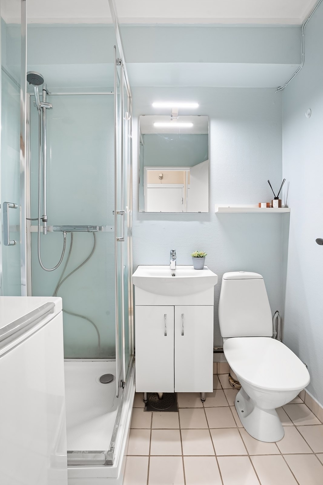 Badet har servantskap med ovenpåliggende servant og ett-greps armatur og speil og belysning over servant. Det er gulvstående toalett og dusjkabinett med hånddusj. Galleribilde