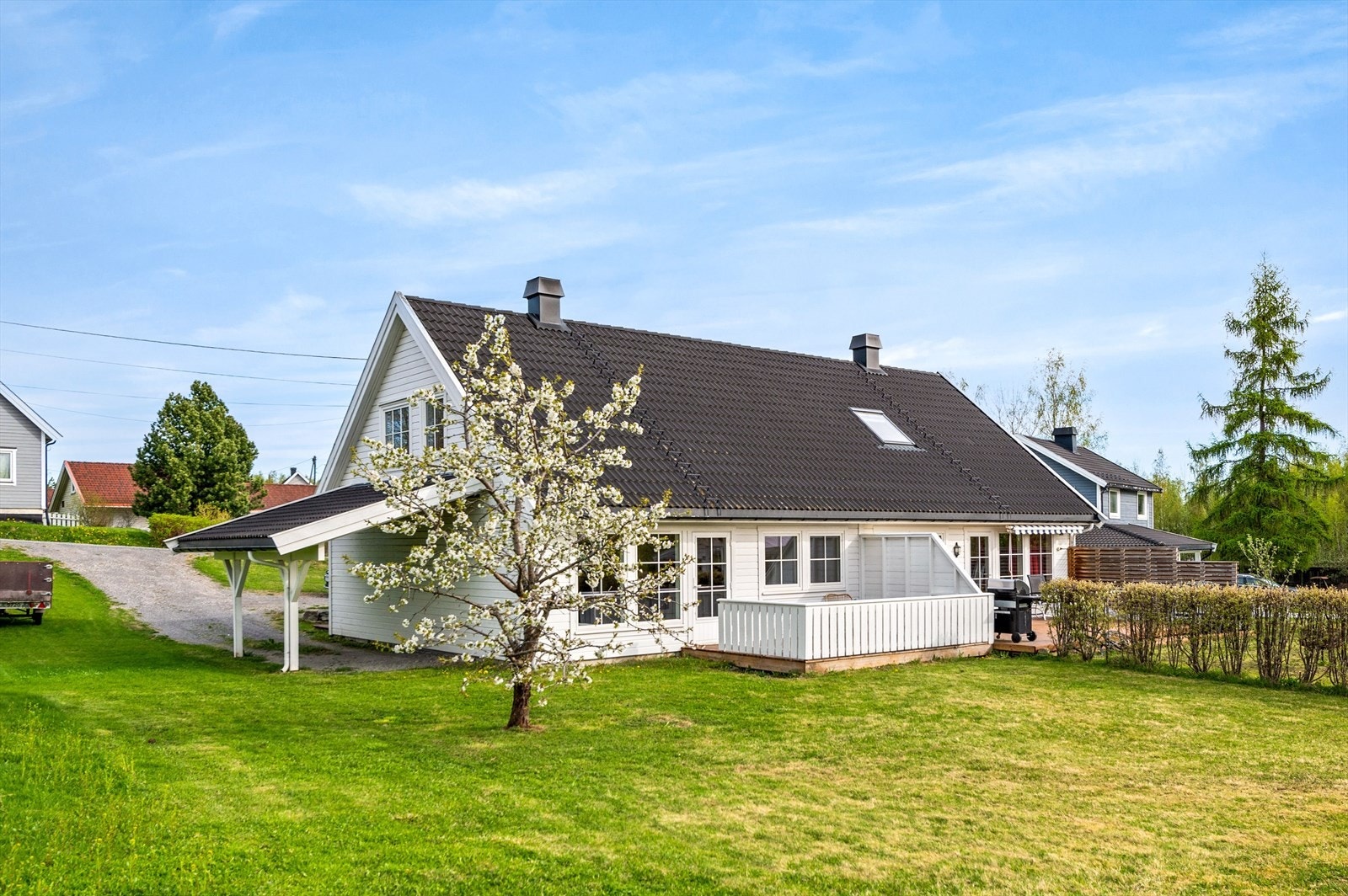 Flat og pent hageareal med hekk mot nabo og noe beplantning. Inntilbygget carport. Galleribilde