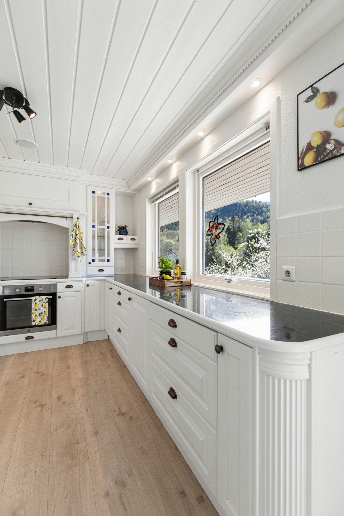 Innredningen inneholder videre laminat benkeplate med flis mot overskap, ventilator, og integrerte hvitevarer; stekeovn/platetopp (2021), oppvaskmaskin og kjøleskap med frysedel. Galleribilde