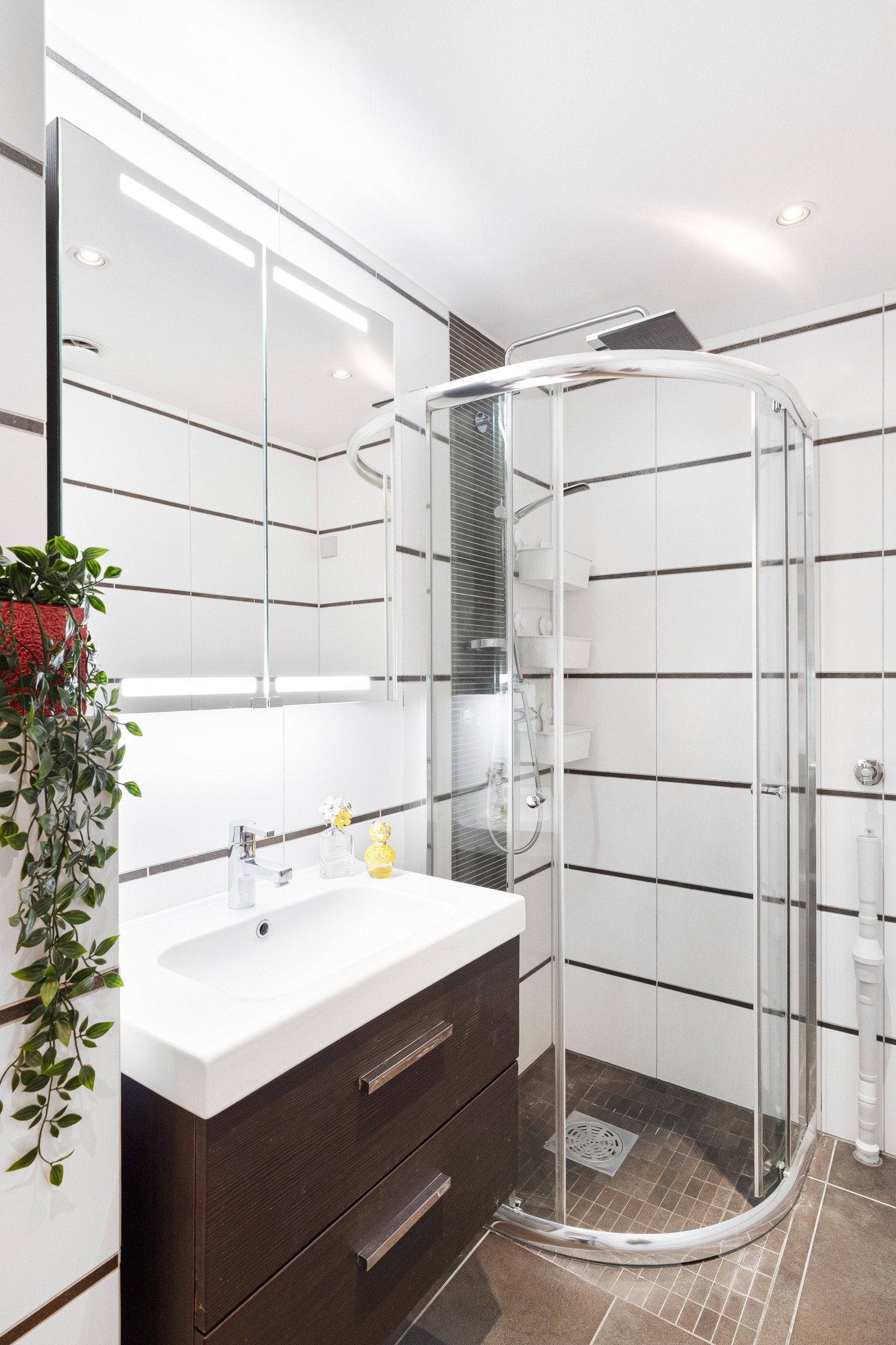 Badet har toalett, varmekabler og et dusjhjørne med skyvedører. Den øvrige innredningen består av servant med svart underskap og et speil med belysning Galleribilde