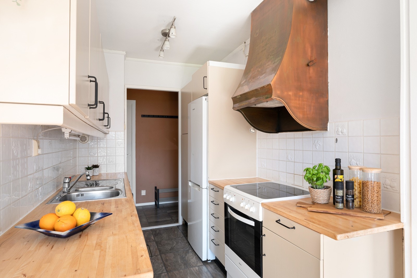 Innredningen er fra IKEA og har slette malte fronter og benkeplate av tre. Over benkplaten er det lyse fliser og over kokesonen er en ventilator installert Galleribilde