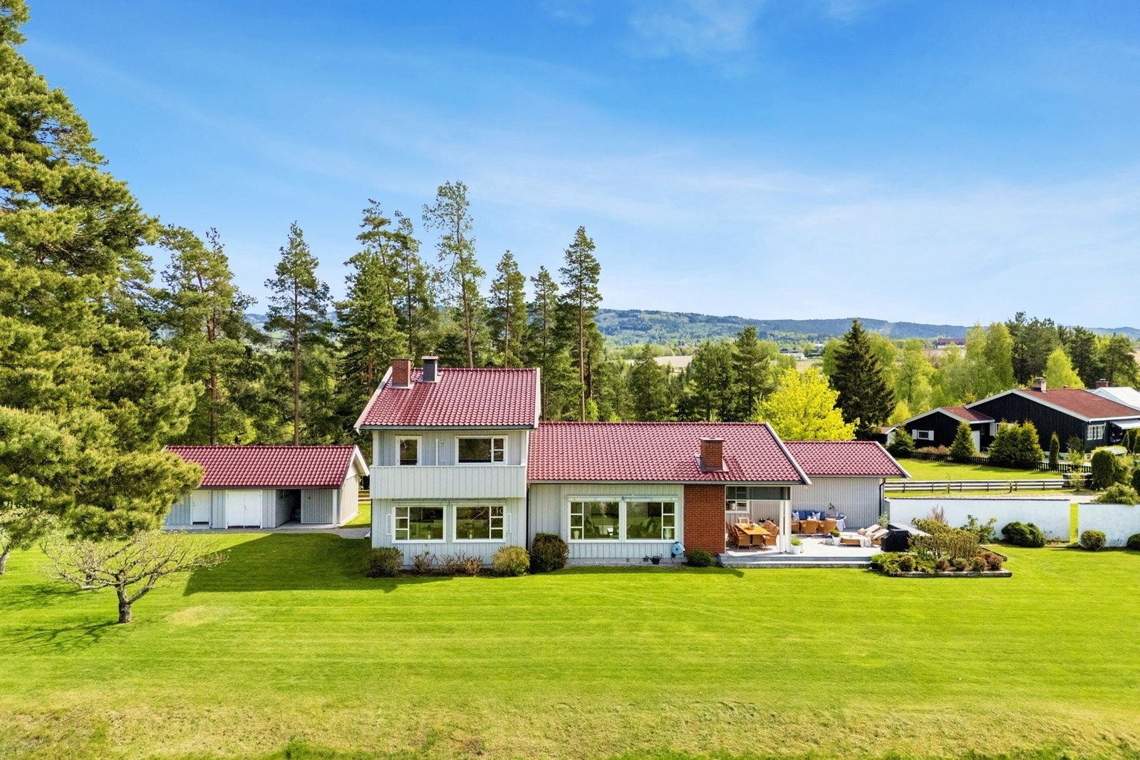 Boligen fremstår velholdt og har en innbydende fasade med rødt tak, lyse panelvegger og store vinduer som slipper inn rikelig med dagslys. Galleribilde