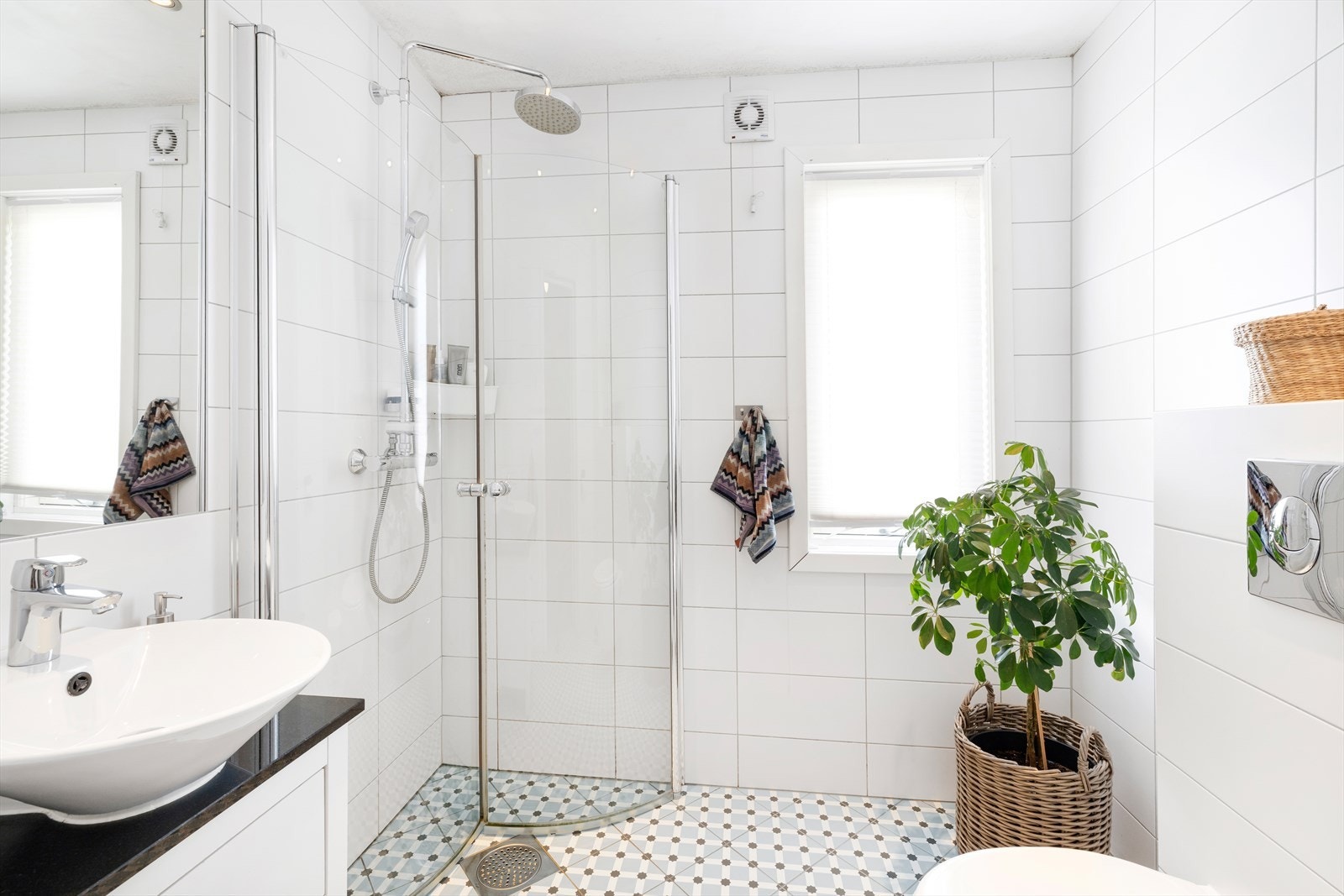 Bad med flislagte gulv og vegger, downlights i tak, dusjhjørne, vegghengt toalett og servant med underskap. Galleribilde