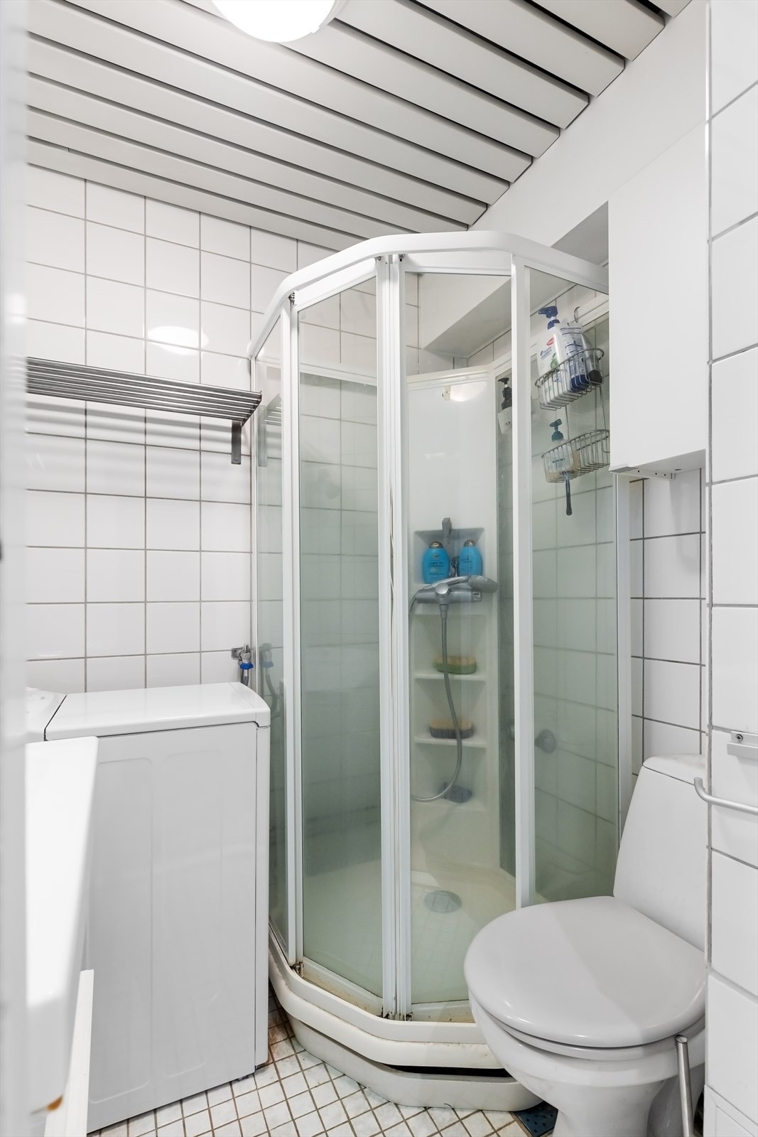 Flislagt bad med dusjkabinett, toalett, opplegg for vaskemaskin og servant Galleribilde