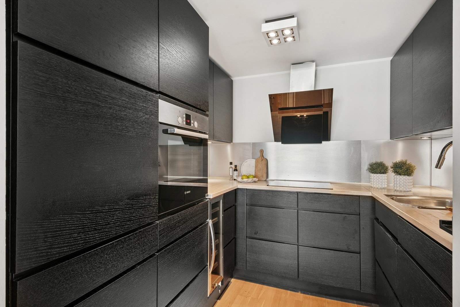 Kjøkkenet har metallplater på veggen over benkeskapene med lys montert under. Benkeplaten er i heltre. Galleribilde