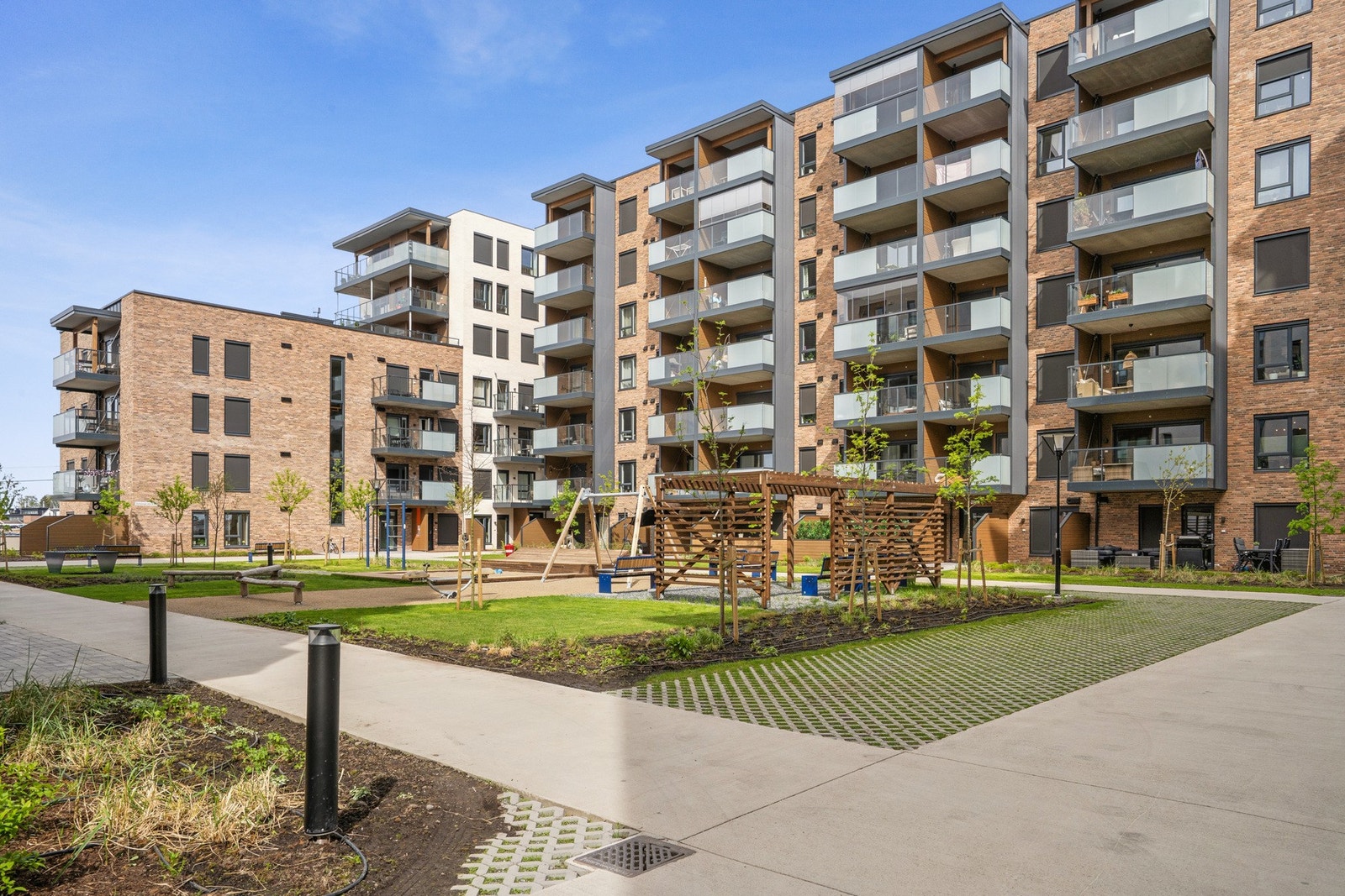 Pent opparbeidet fellesområde med grønne plener, lekeapparater og sosiale soner. Galleribilde