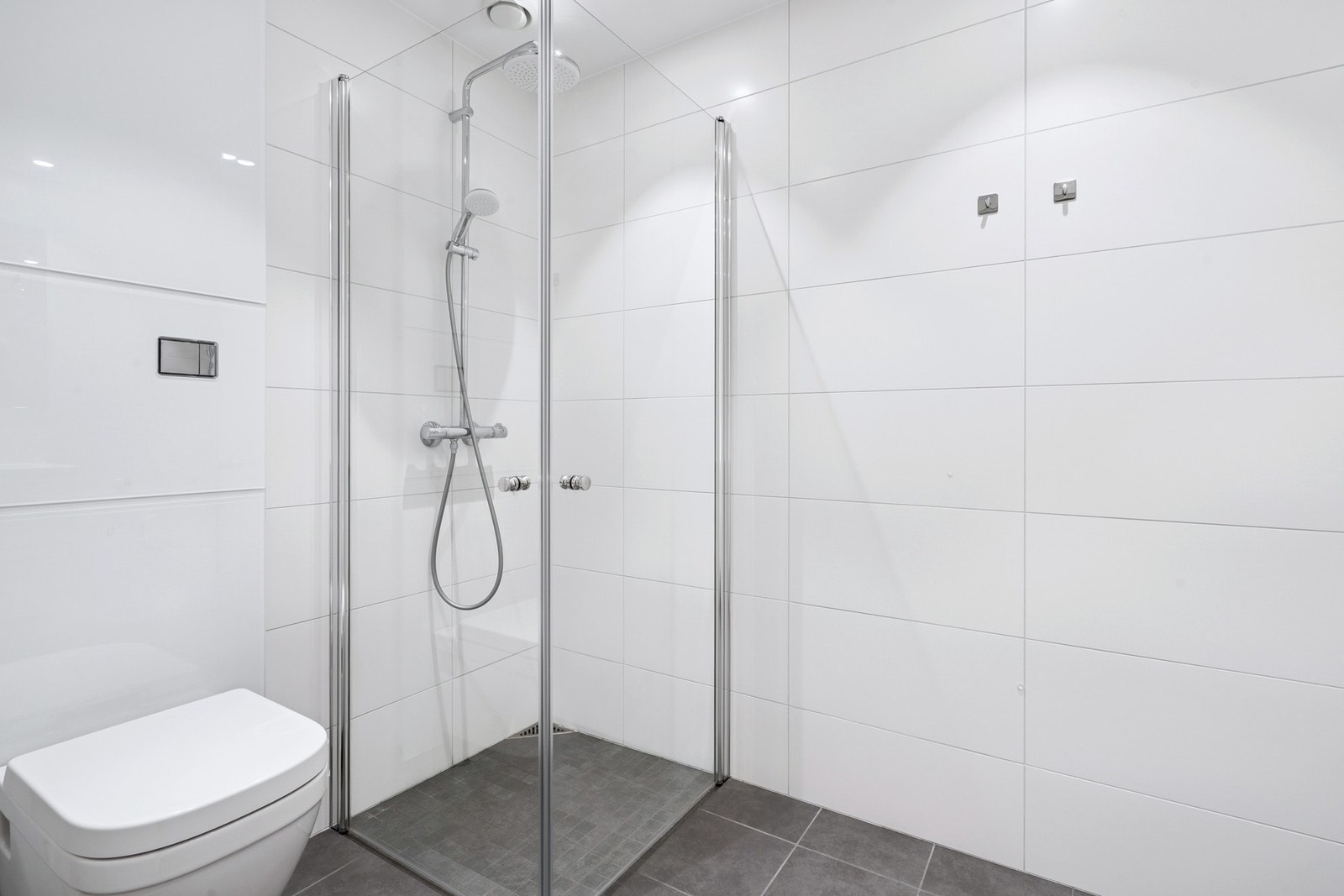 Flislagt bad med dusjhjørne, vegghengt toalett og gulvvarme for ekstra komfort. Praktisk løsning med god plass og tidløst uttrykk. Galleribilde