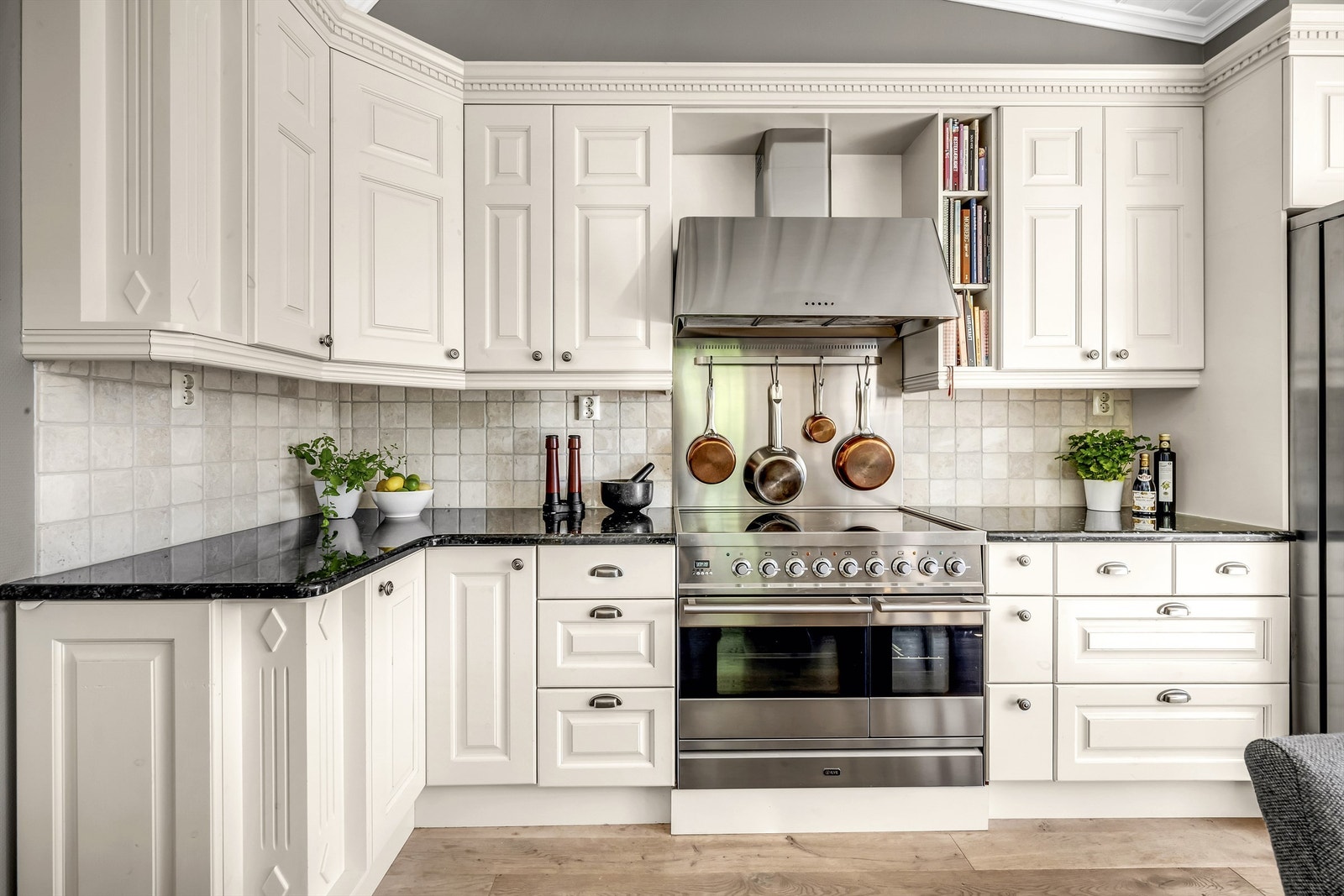 Benkeplate i sten, lekre detaljer på kjøkkenfrontene, kjøle-/fryseskap med isbitdispenser og stor komfyr med keramisk platetopp Galleribilde