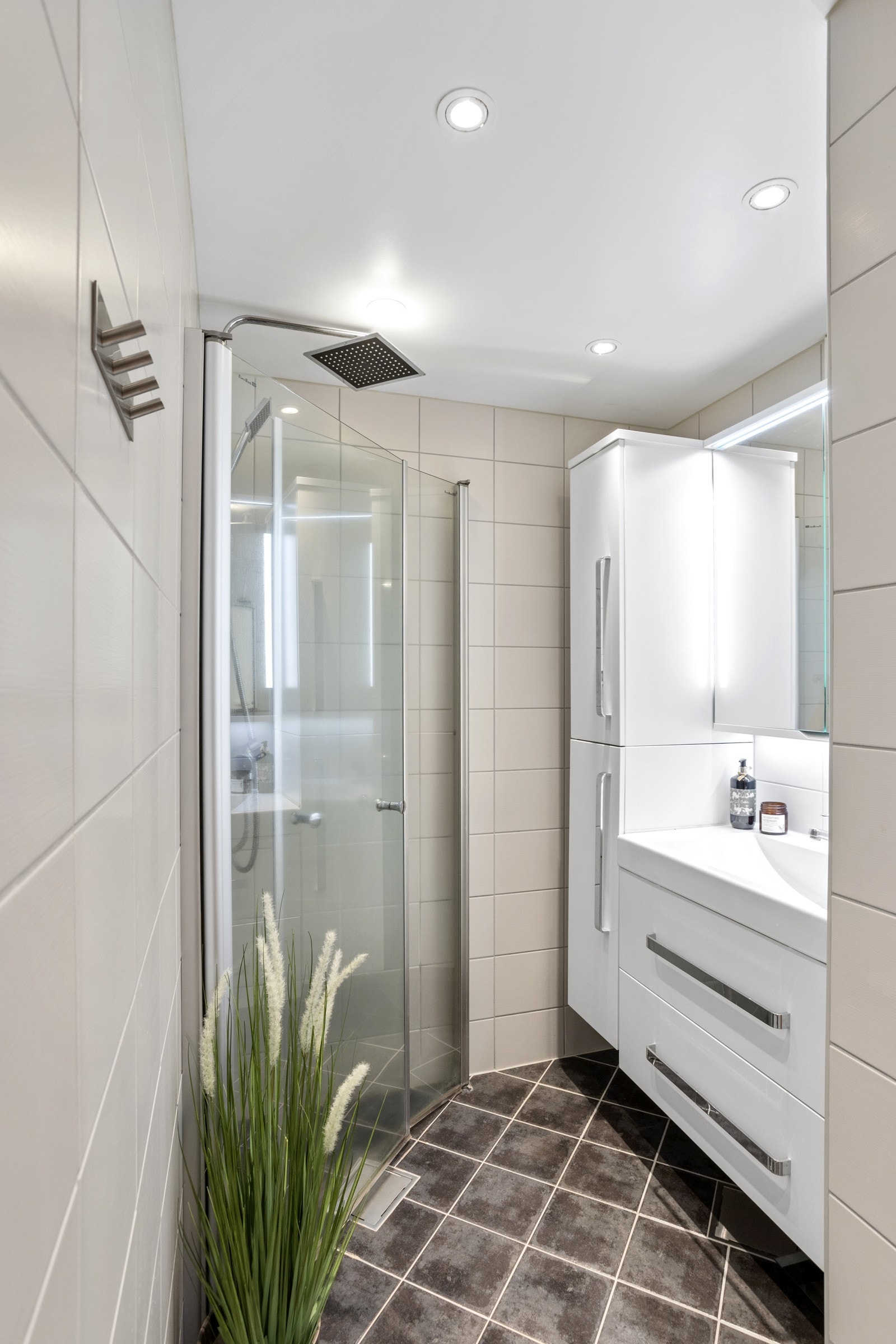 Baderomsinnredningen består av et dusjhjørne med glassdører som slår innover når dusjen ikke er i bruk. Vegghengt toalett, vegghengt skap- og servantinnredning med skuffer Galleribilde