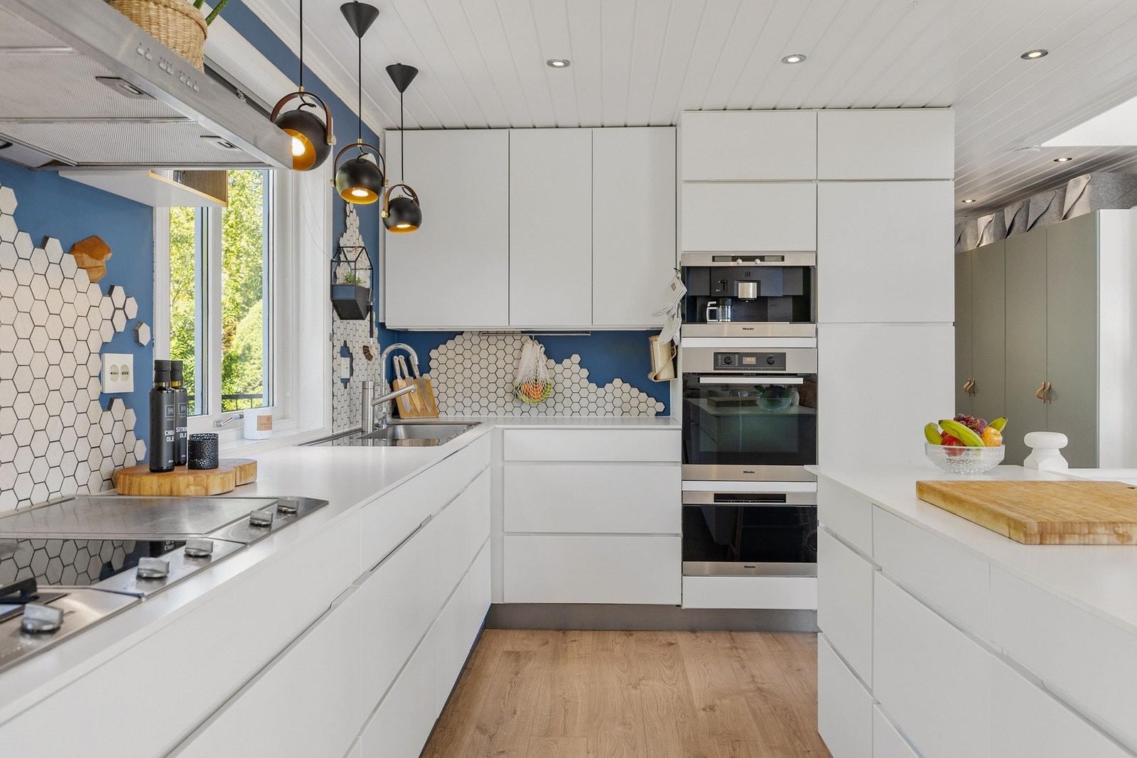 Det er benkeskapsbelysning og stikkontakter over kjøkkenbenken, samt fliser på vegg mellom benk og overskap Galleribilde