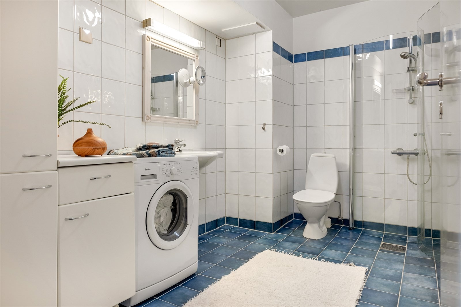 Badet er innredet med dusjhjørne, toalett, benkeskap med nedfelt servant og speil med belysning over. Opplegg for vaskemaskin Galleribilde