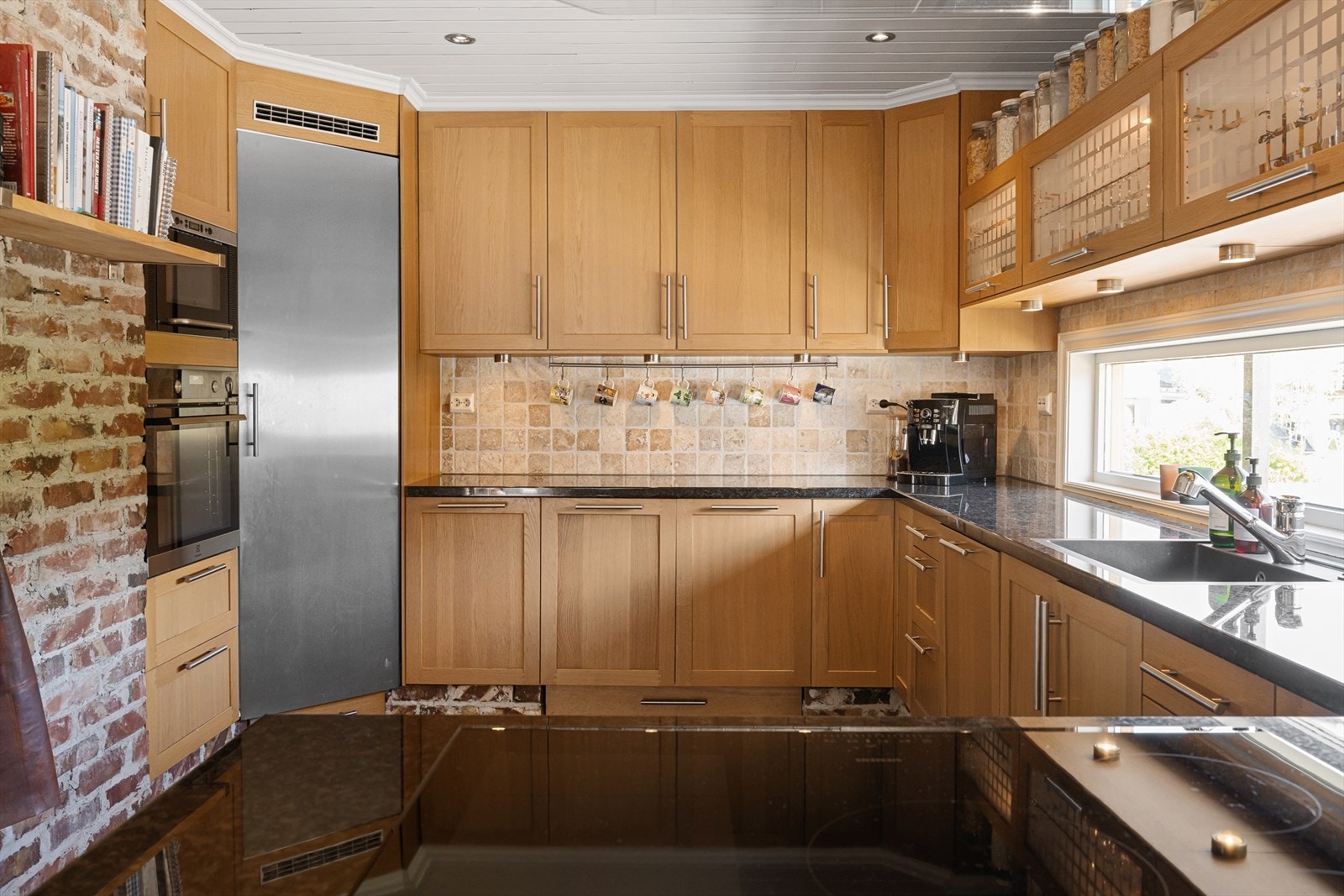 Kjøkkenet er videre utstyrt med kjølehjørne og integrerte hvitevarer. Stilig detalj med murstein i sokkel. Sentralstøvsugeren har også feieluke under skuffer ved komfyr. Galleribilde