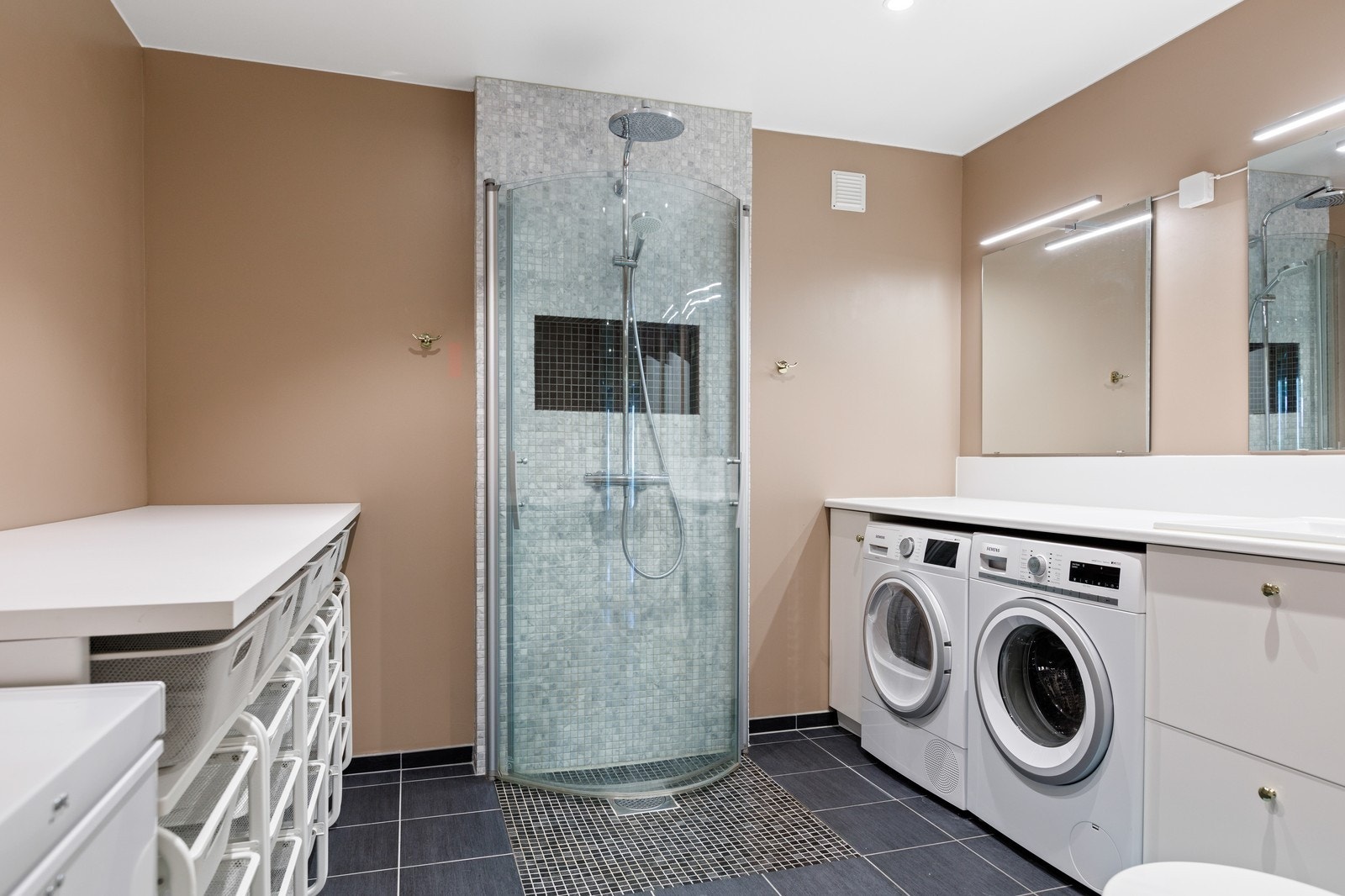 Stilrent og praktisk innredet hovedbad med vaskemaskin og tørketrommel Galleribilde