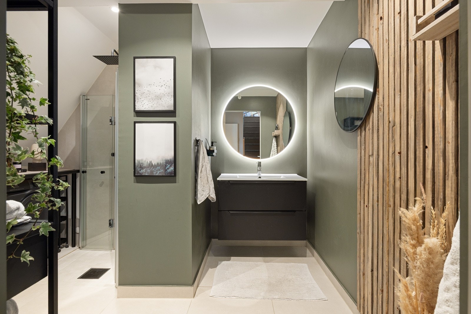 Moderne baderomsinnredning med sorte skuffer og lys heldekkende servant, stort rundt speil med integrert belysning over. Galleribilde