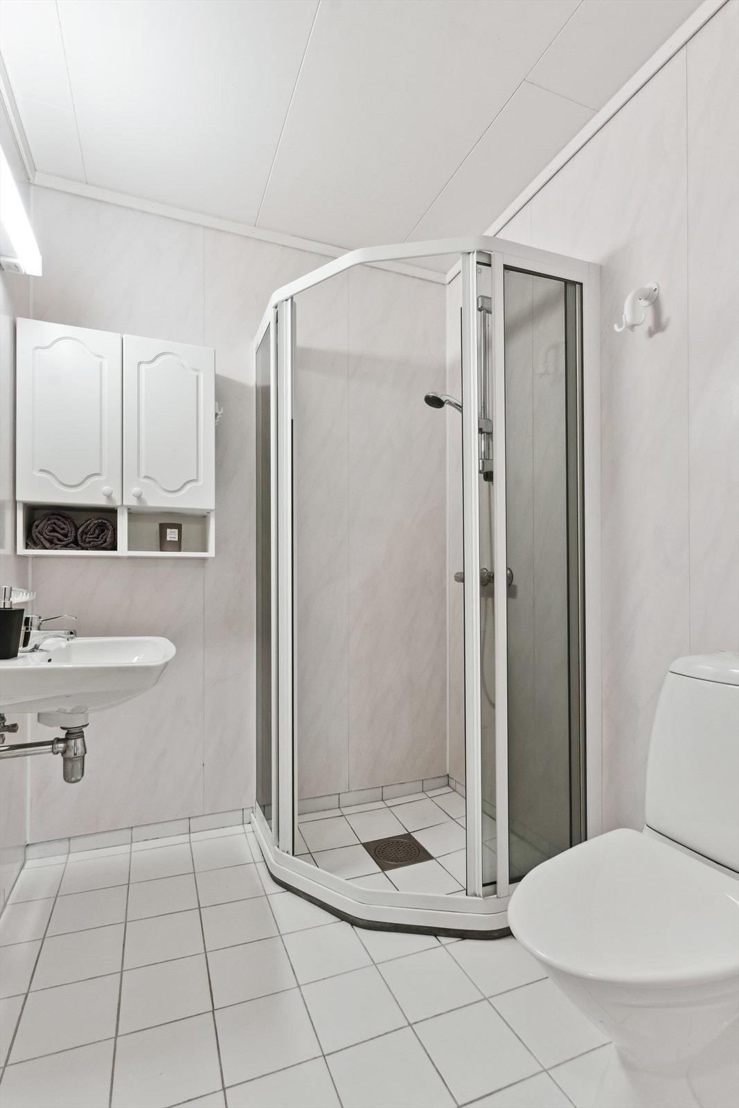 Badet i underetasjen held noko eldre standard, med varmekablar i golv, toalett, servant, dusj og enkel kvit innreiing. Galleribilde