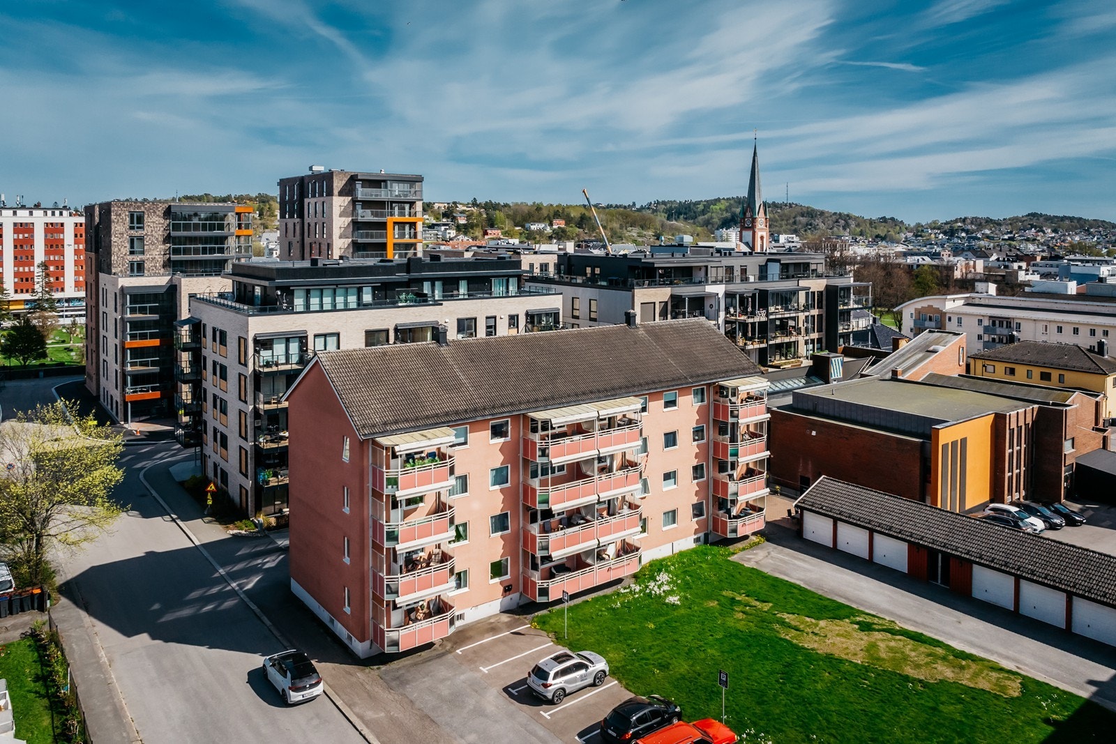 Fasaden av bygget og felles plen. Parkering for beboere. Her har man ikke en fast plass, men et p.bevis i ruten også står man der man finner ledig plass. Galleribilde