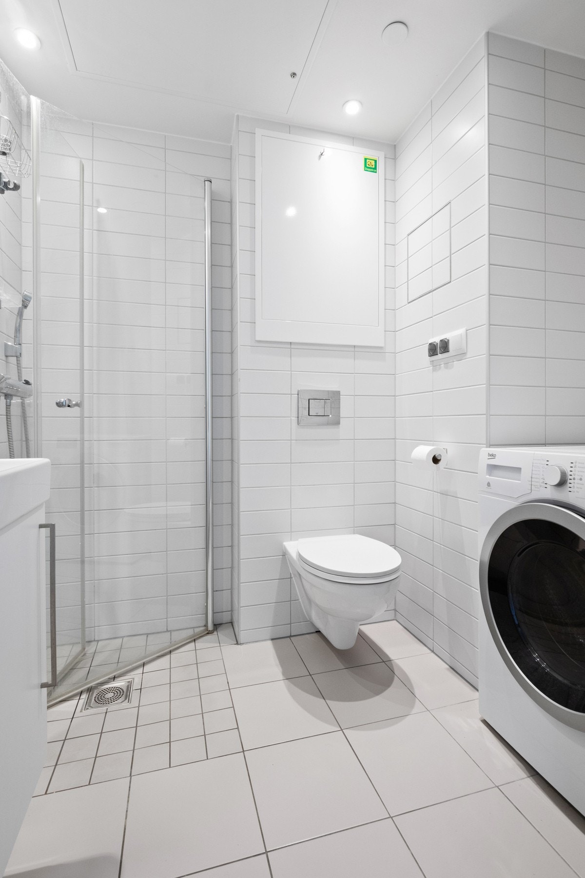 Videre har badet et vegghengt toalett, opplegg for vaskemaskin og et dusjhjørne med innfellbare glassdører. Galleribilde